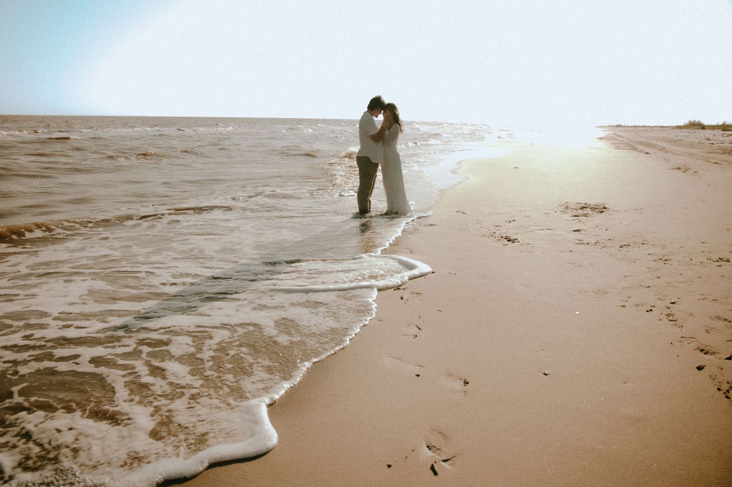 A silhouetted figure walks along a misty beach shoreline as waves roll in during golden hour.