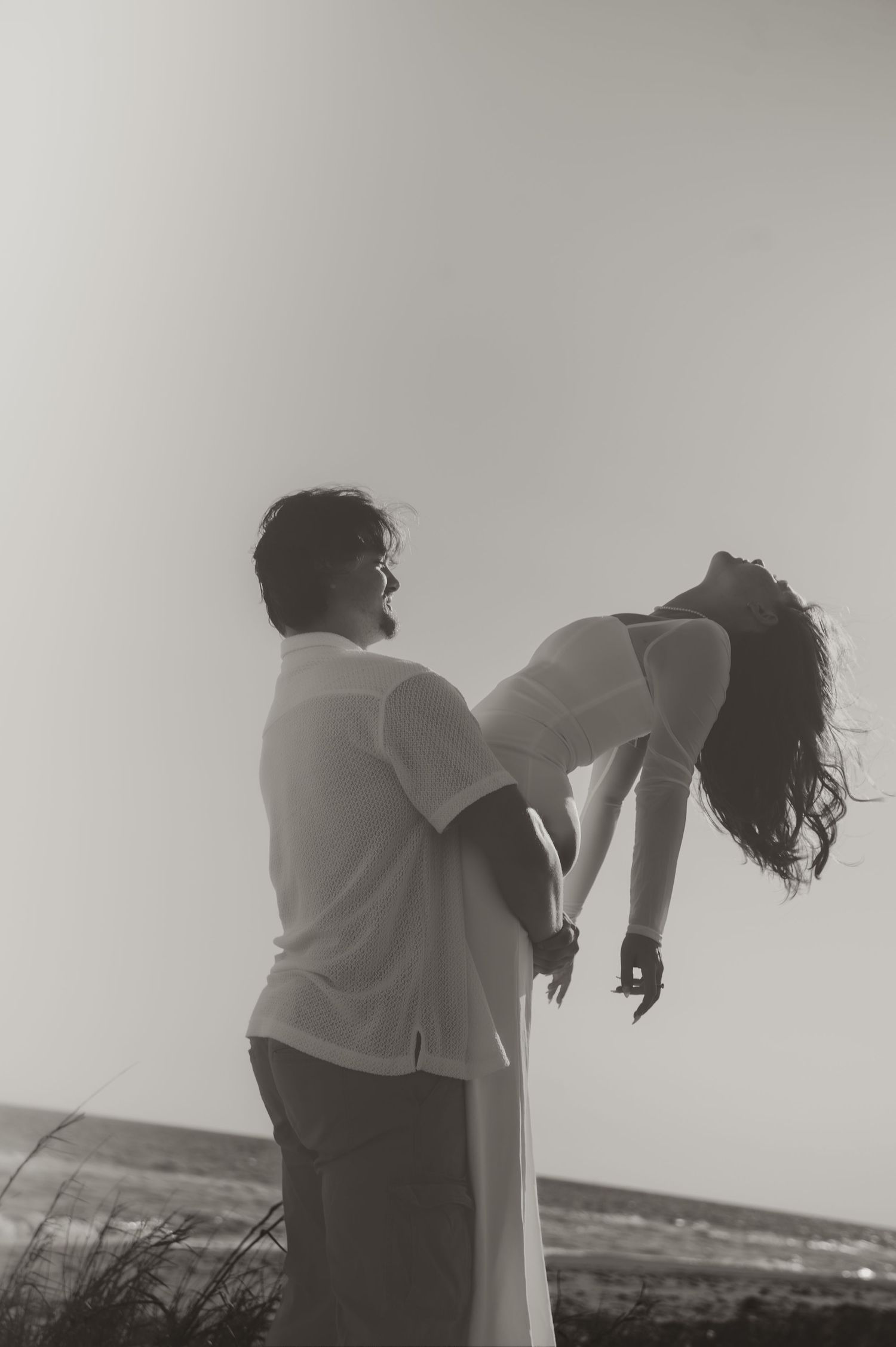 A romantic black and white silhouette of two people embracing in a meadow with one person dipping the other.