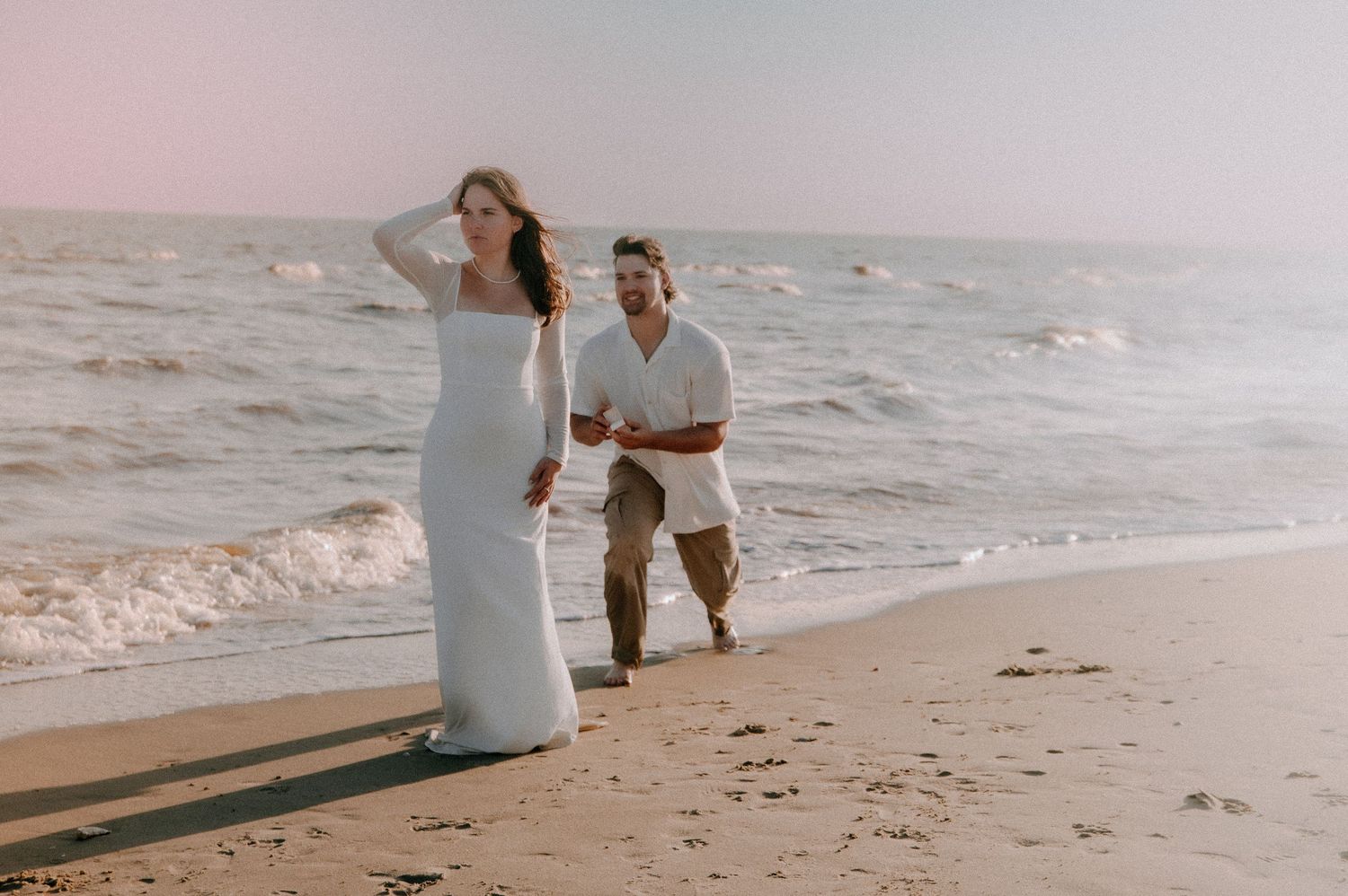 A couple sharing a romantic proposal moment on a sunset beach with waves crashing in the background.