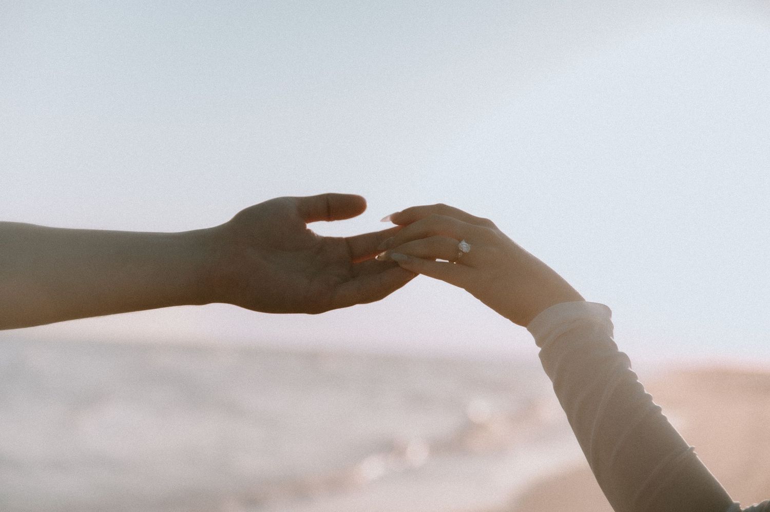 A romantic proposal moment taking place on a sandy beach with brown waves and cloudy sky in the background.