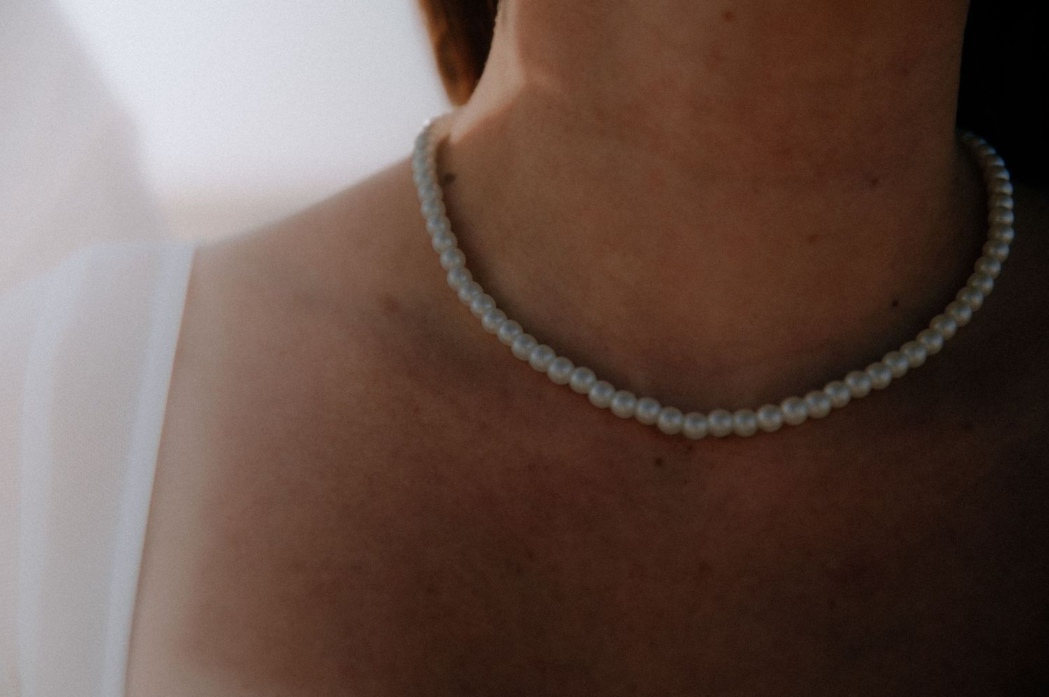 A person models a delicate beaded choker necklace with a round pearl pendant on a neutral background.