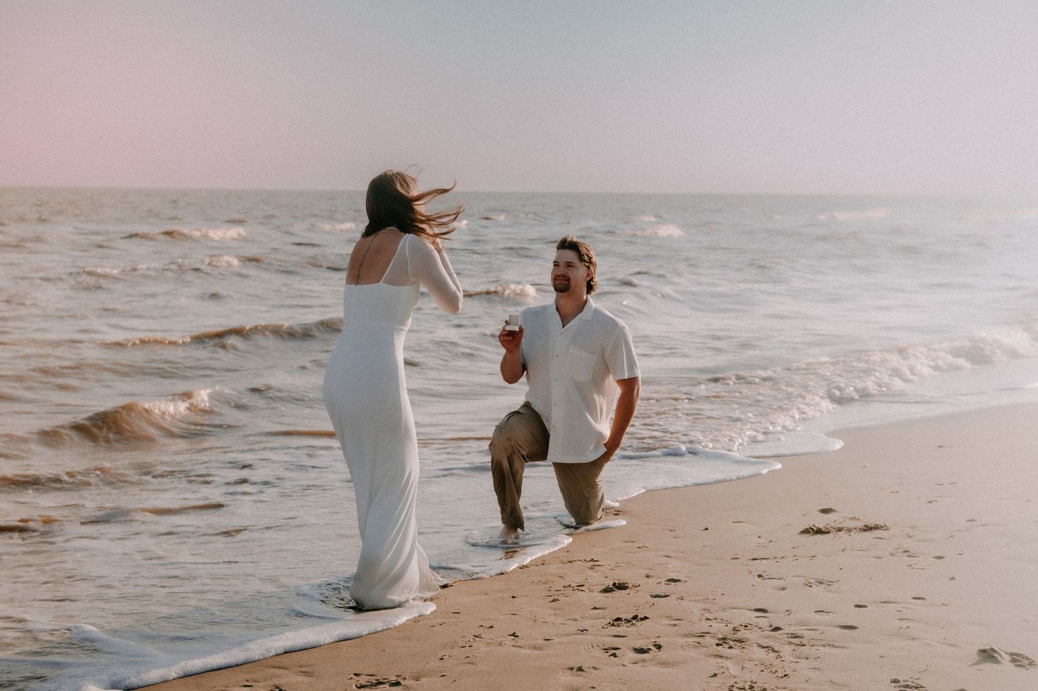 A proposal scene unfolds on a peaceful beach at sunset with gentle waves crashing in the background.