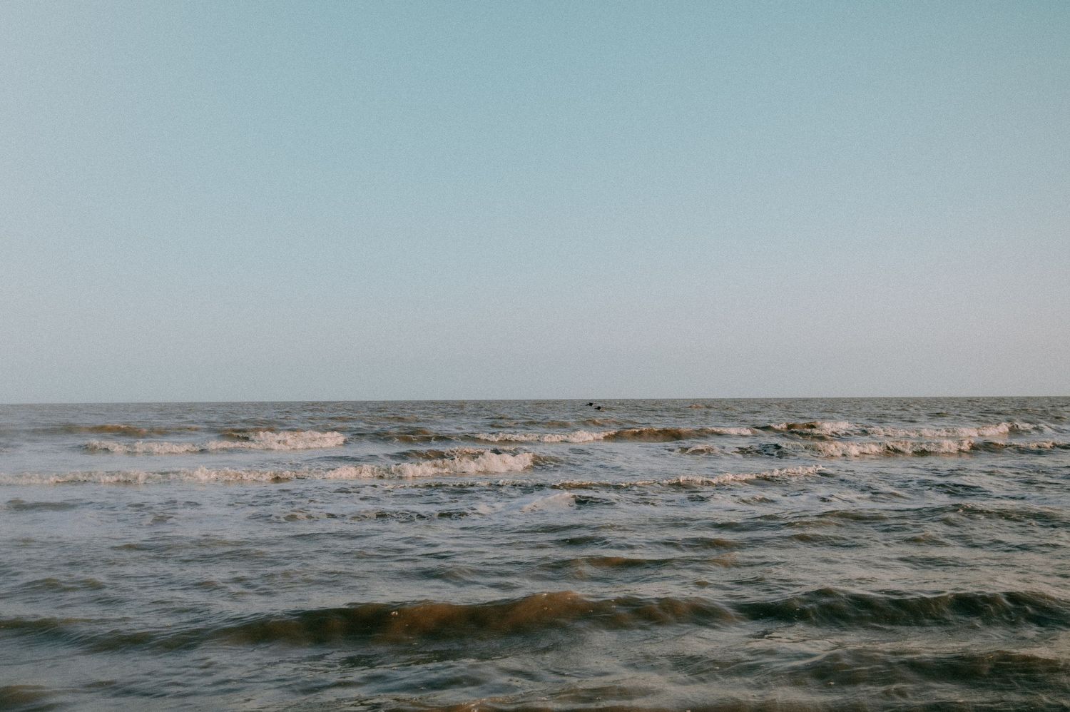 Panoramic seascape showing waves rolling into shore under a bright blue sky.