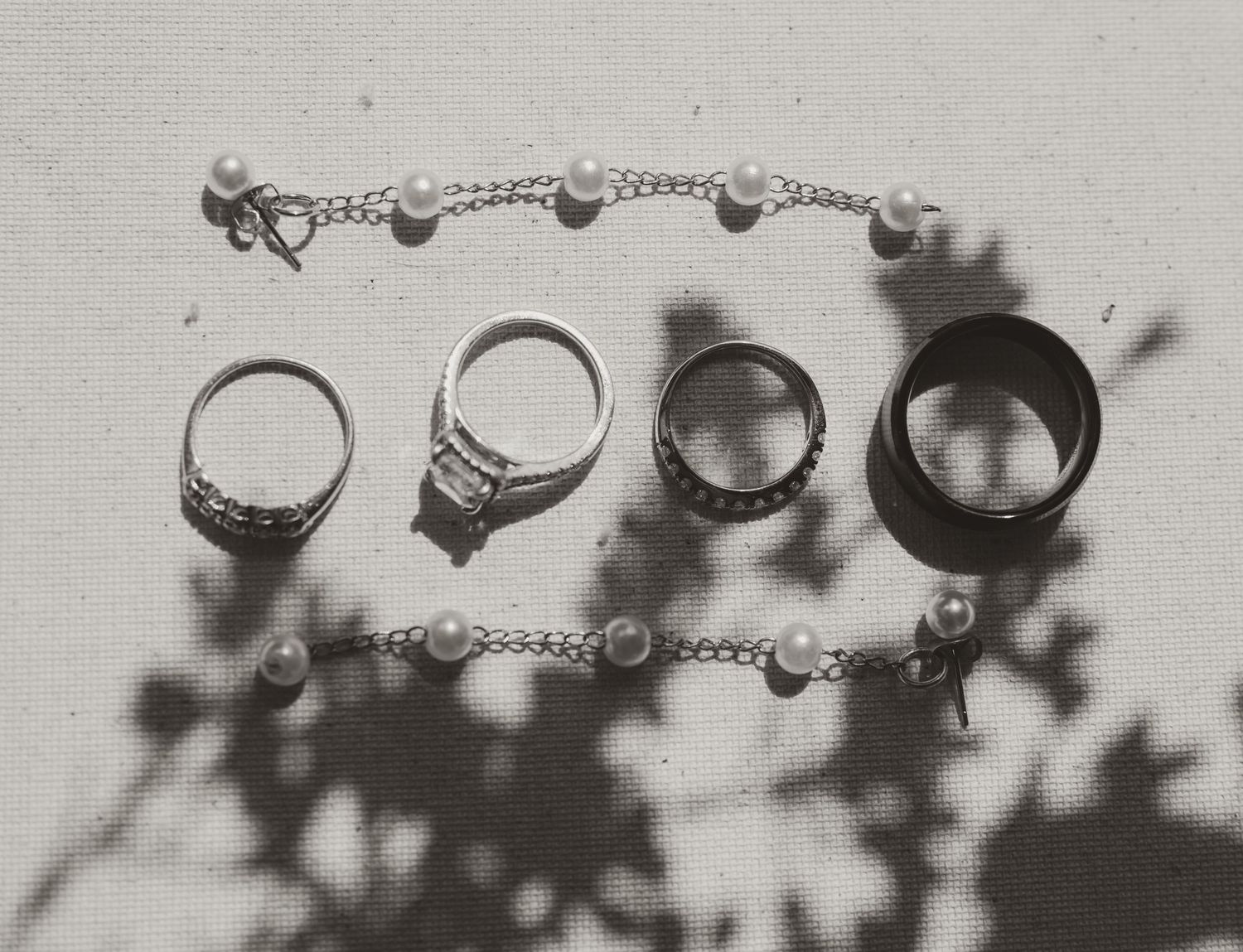 A black and white artistic macro photograph shows delicate blossoms and foliage alongside wedding rings.