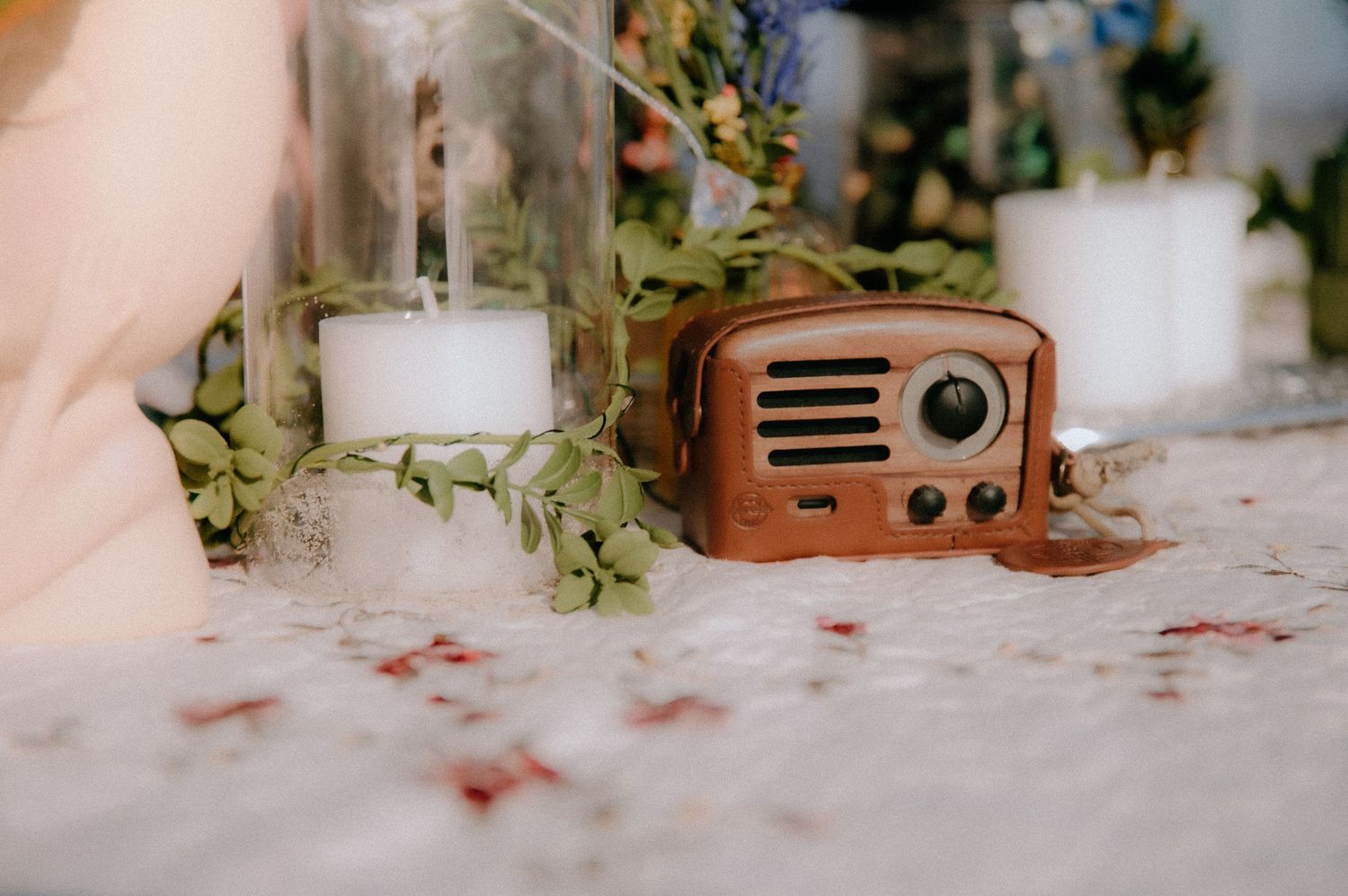 A vintage wooden radio sits on a white surface next to glass containers and green foliage decor.
