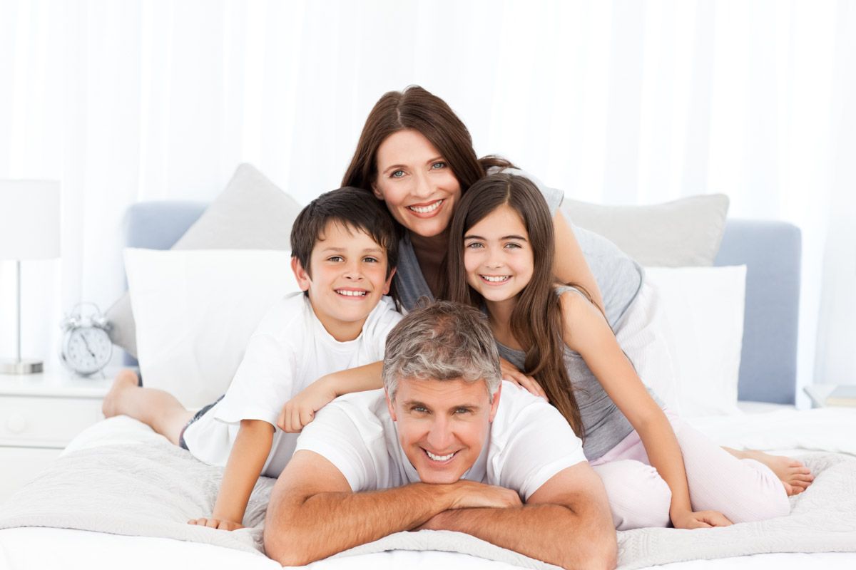 Family of four posed on bed for professional portrait.