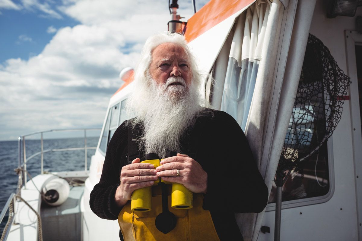 Fisherman on fishing boat in Cork holding binoculars looking out to sea.