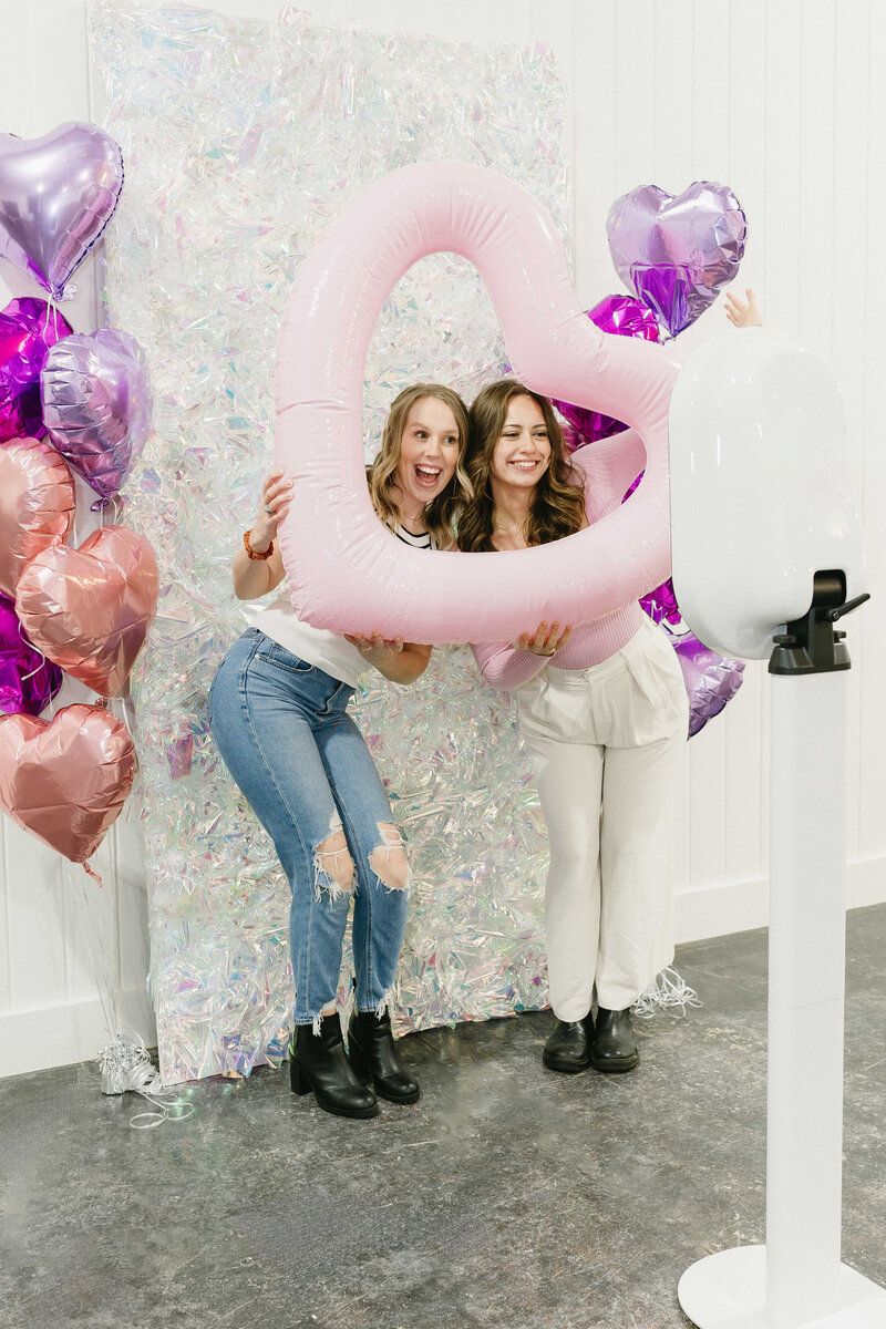 Friends playing with pink and purple heart balloons against a sparkly silver backdrop.