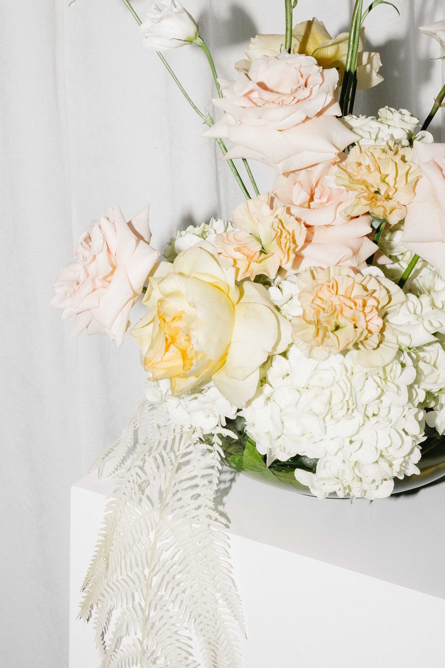 Delicate bouquet of blush pink roses and white hydrangeas arranged on a white table with fern details.