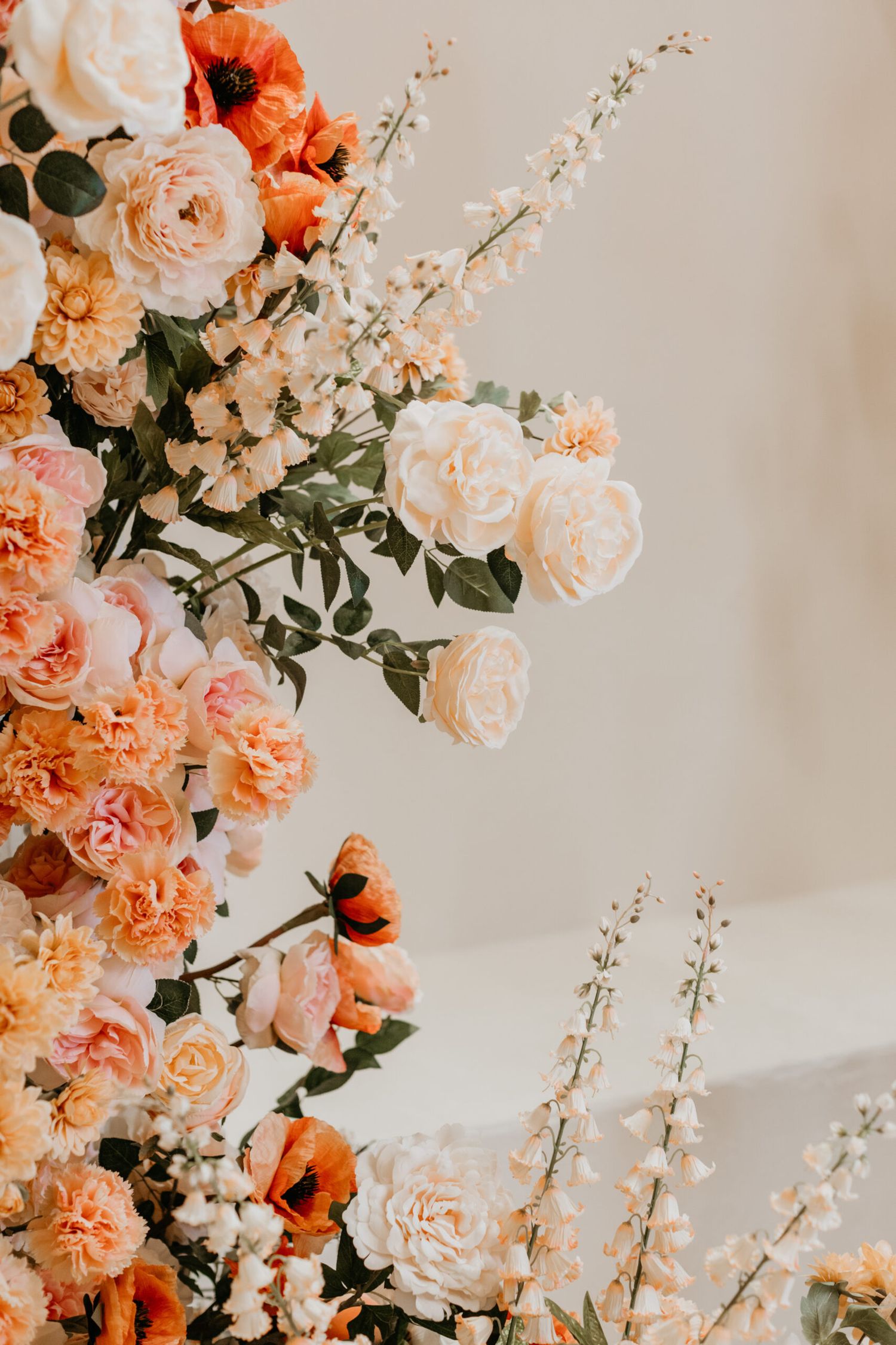 Close-up of coral and peach roses with greenery against neutral background.