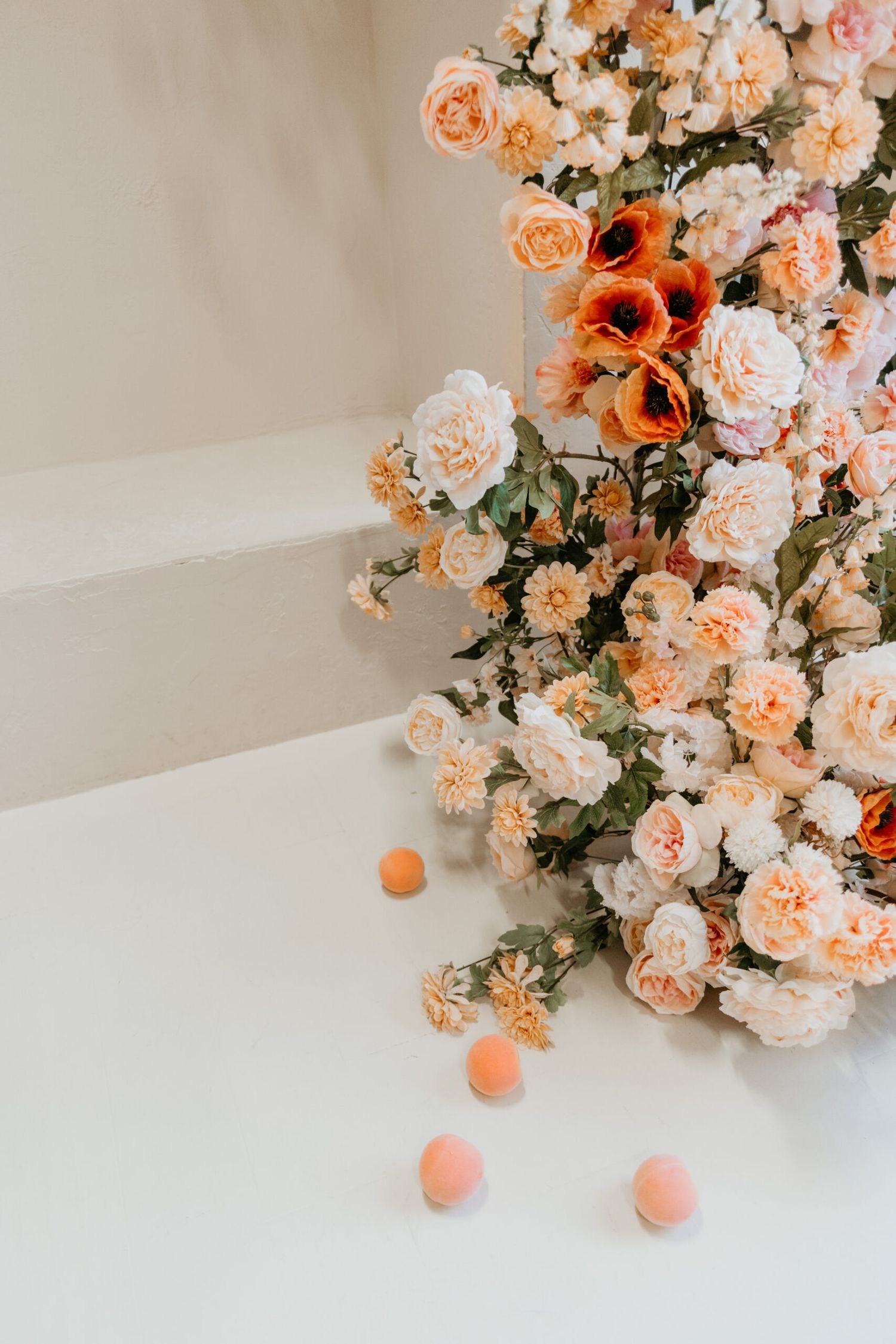 Elegant floral arrangement with peach and coral roses cascading along a white surface.