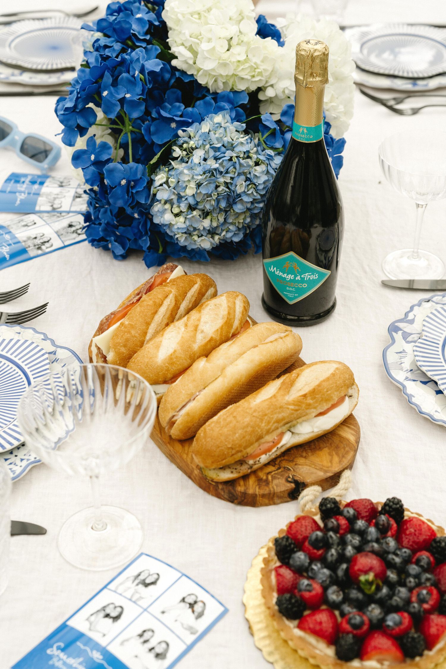 Elegant table setting with fresh berries, bread, blue hydrangeas and champagne bottles.