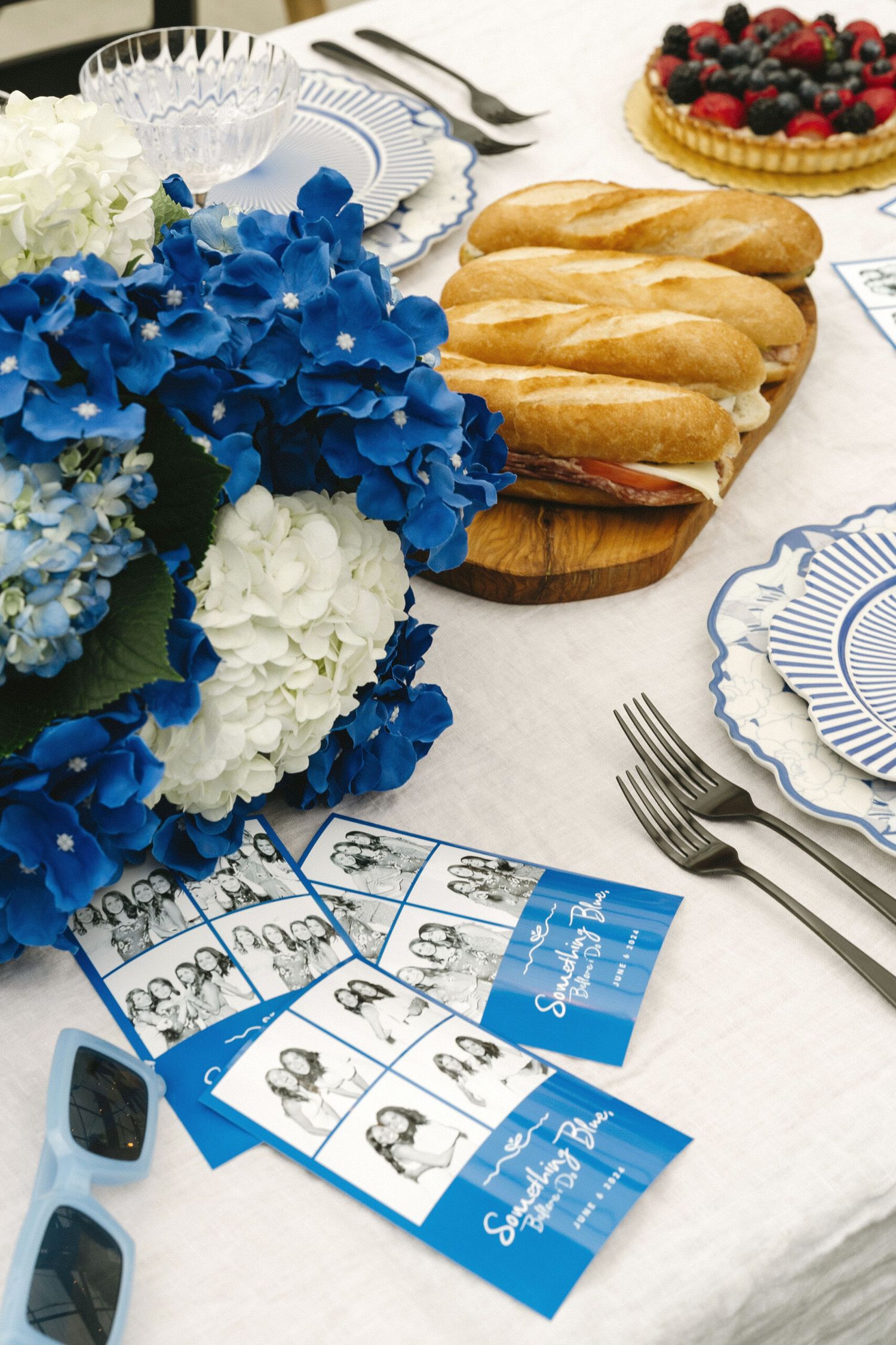 Table decorated with blue hydrangeas, bread, berries and custom photo cards for a special event.