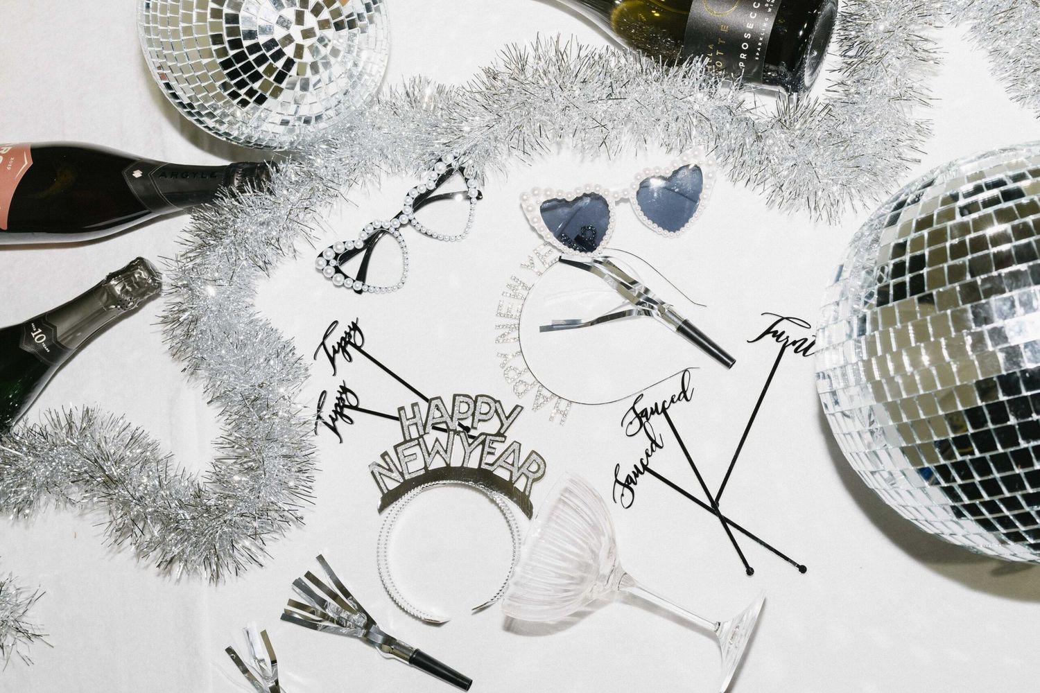 Party decorations including disco balls, tinsel garland, and cocktail glasses arranged on white background.