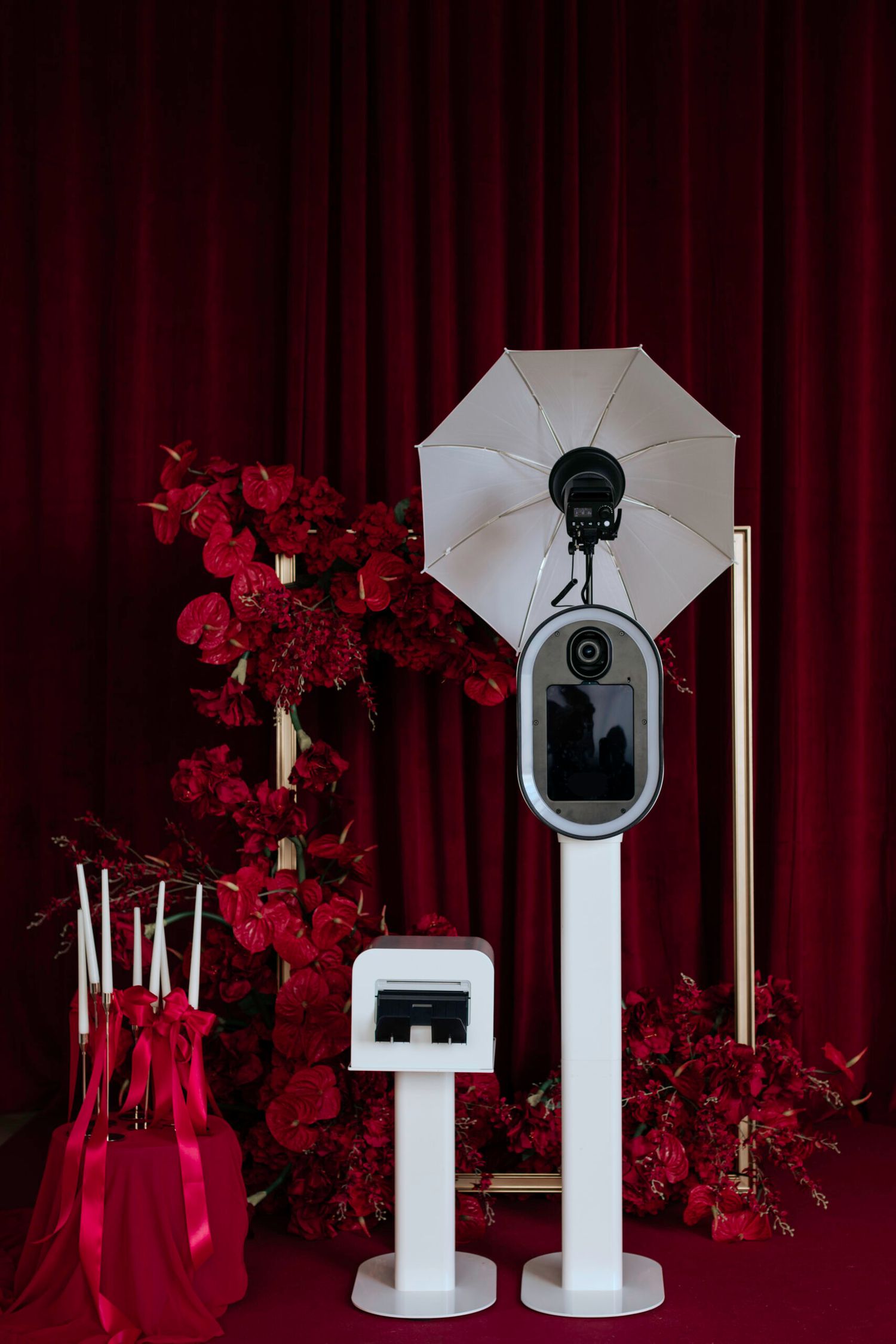 Photography lighting setup with white umbrellas and stands against a red curtain backdrop.