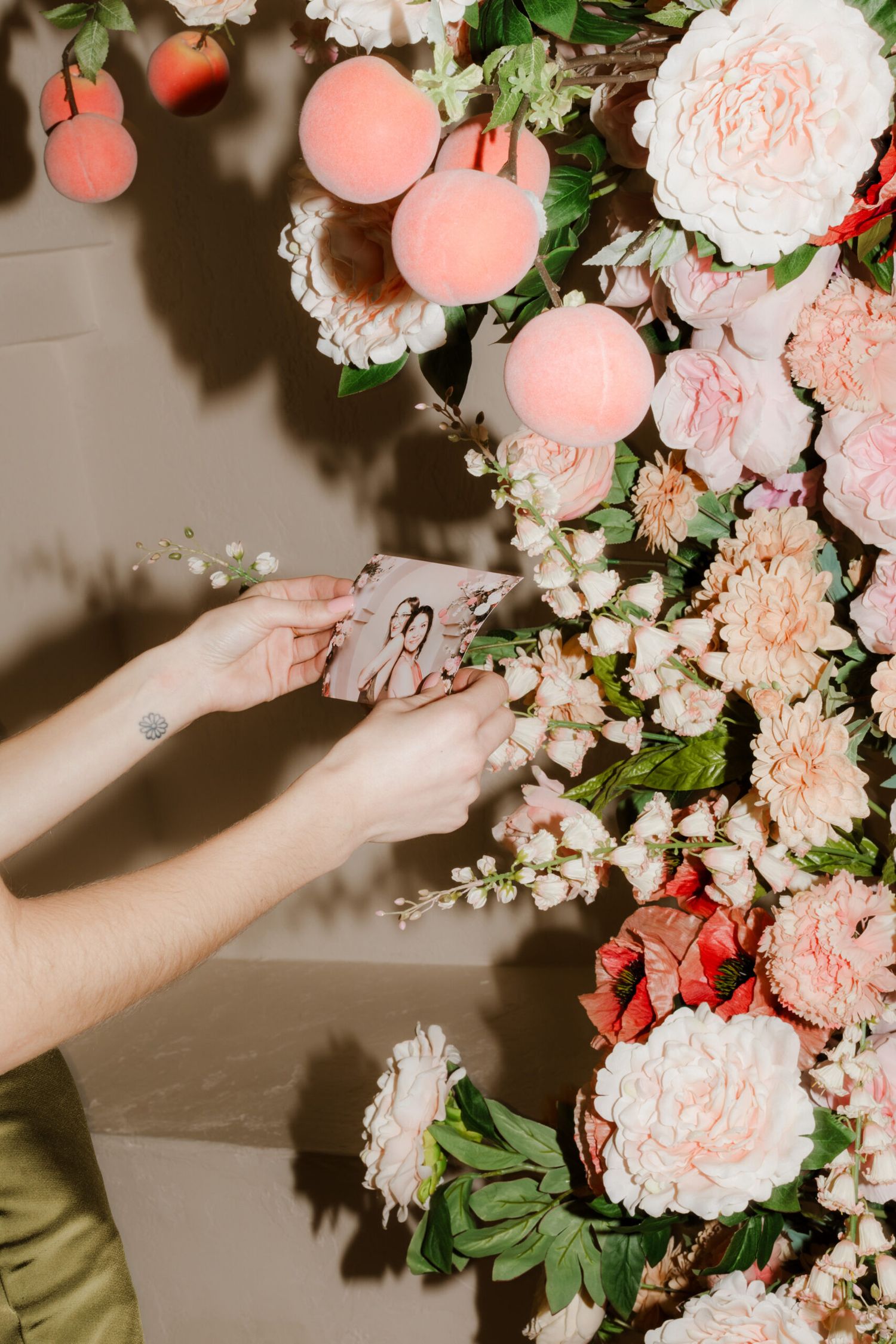 Close-up of hands arranging delicate pink and coral flowers in a luxurious floral installation.