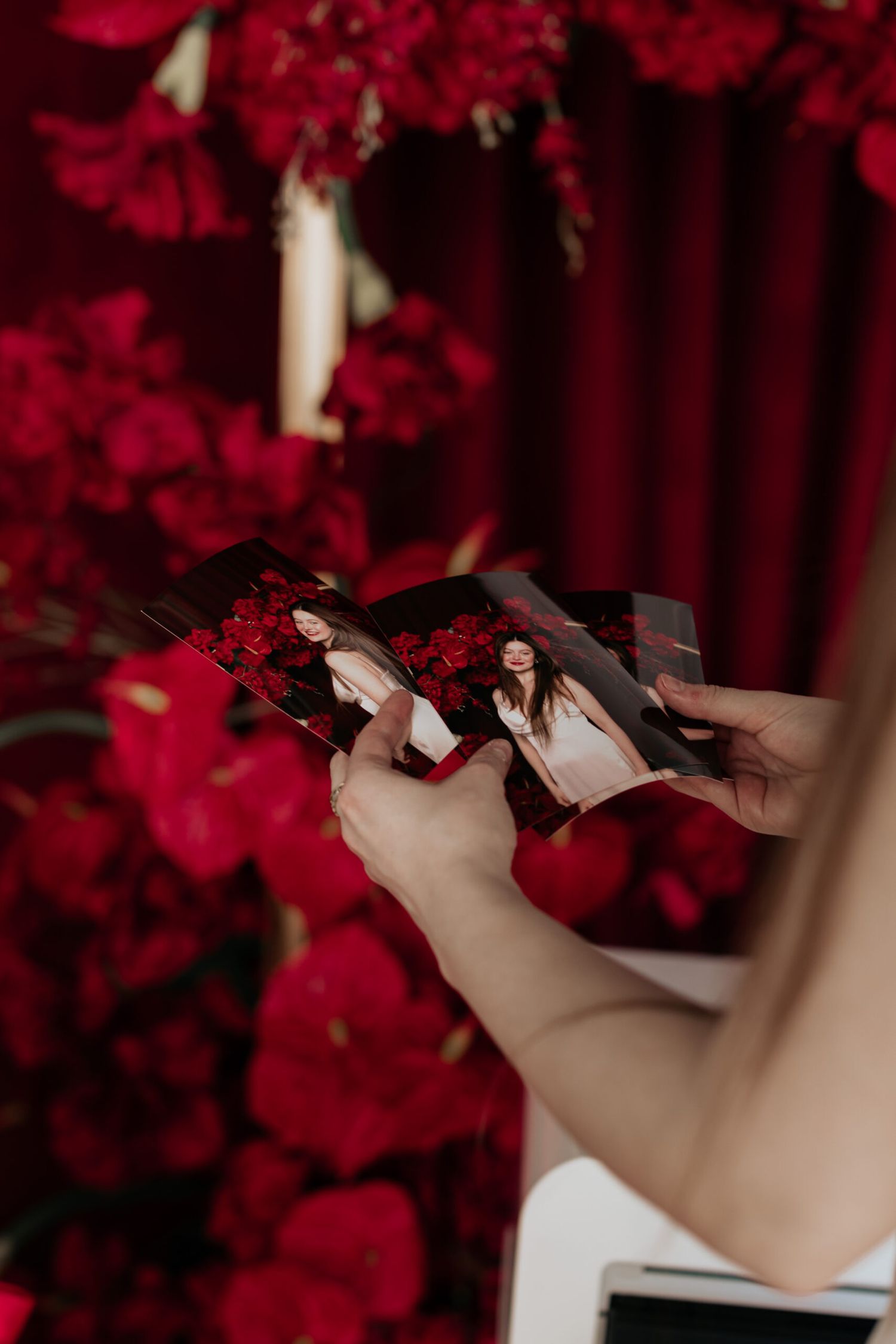 Hands adjusting camera settings in front of lush red floral backdrop.