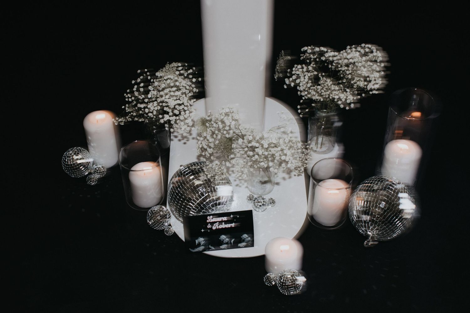 Dark moody arrangement of white candles and decorative elements against black background.