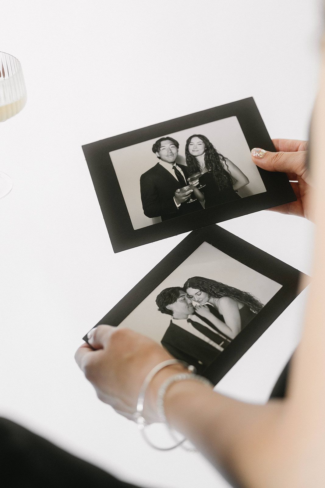 Hands holding multiple black and white photographic prints being sorted on a bright white surface.