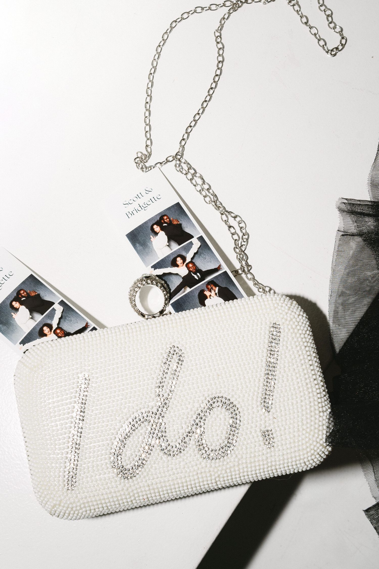 White pearl-encrusted cylindrical clutch purse with chain strap displayed against gray background.