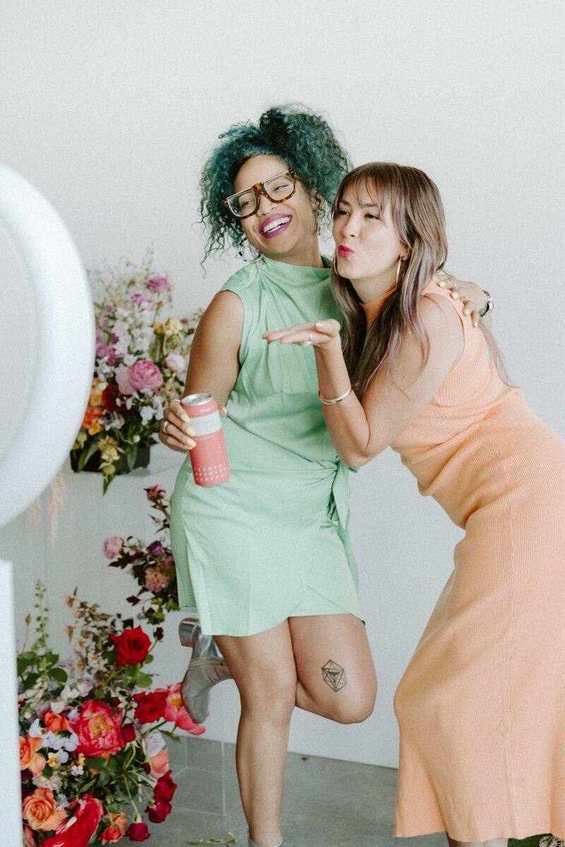 Two people in mint green and peach outfits pose playfully together with floral decorations.