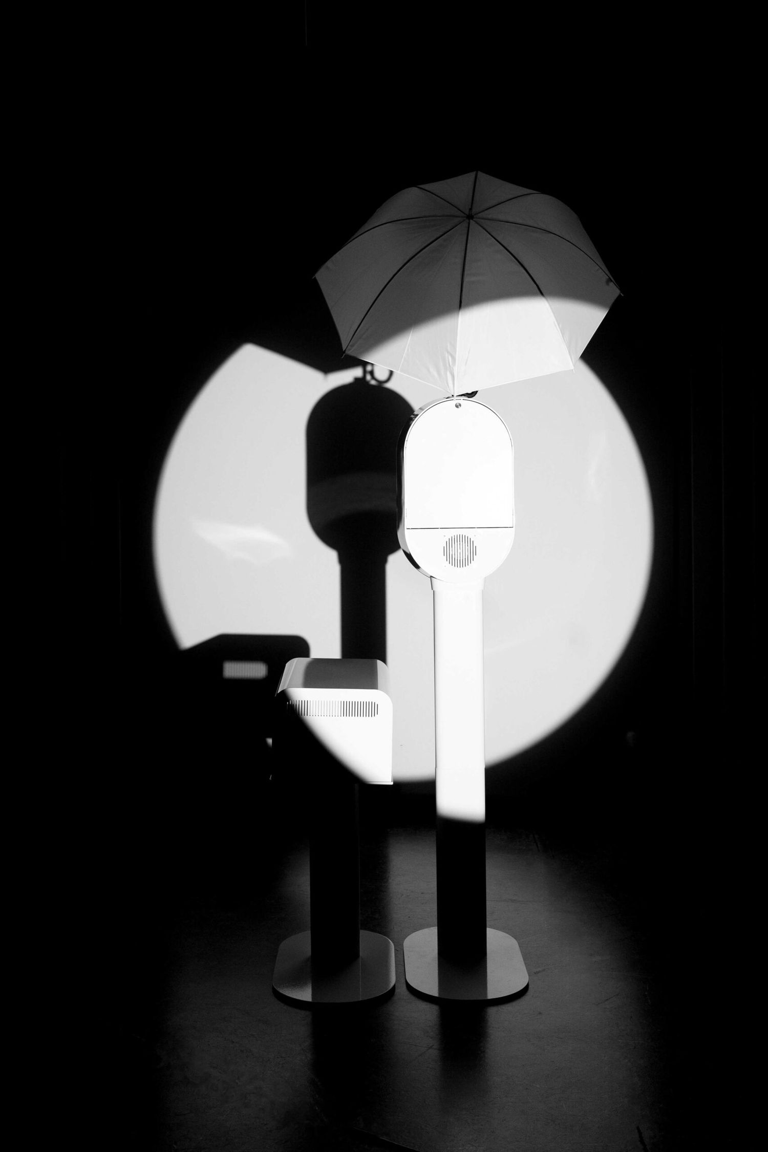Dramatic black and white lighting setup with umbrella and studio equipment silhouettes.