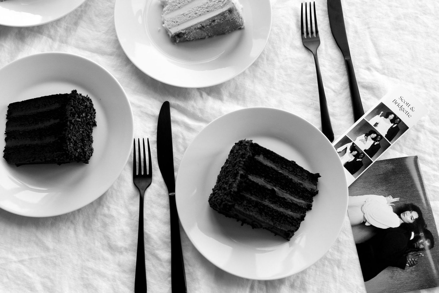 Minimalist black and white photograph of chocolate cake slices on multiple plates with forks.