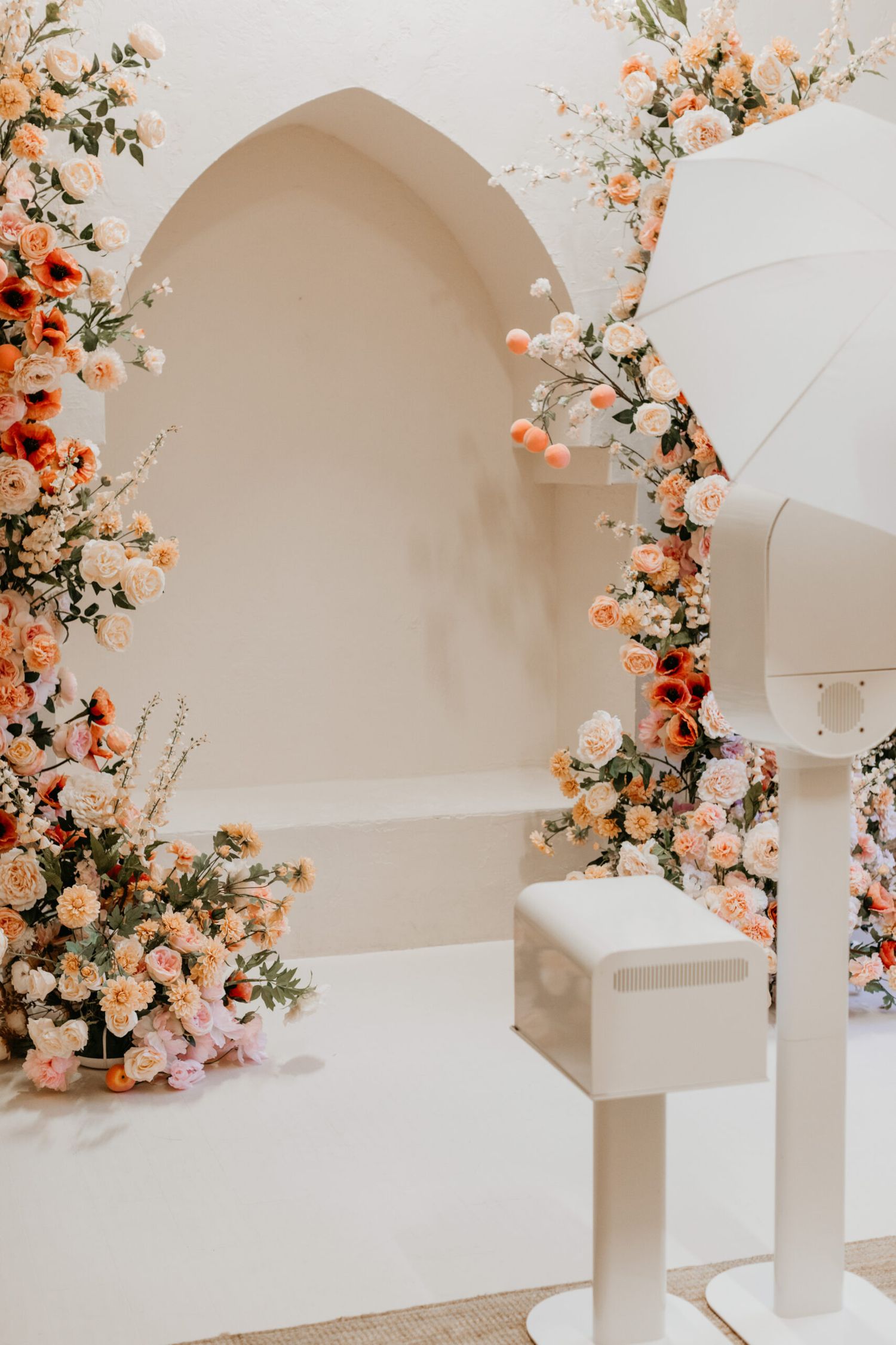 Elegant archway decorated with peach and orange floral arrangements in a white venue.