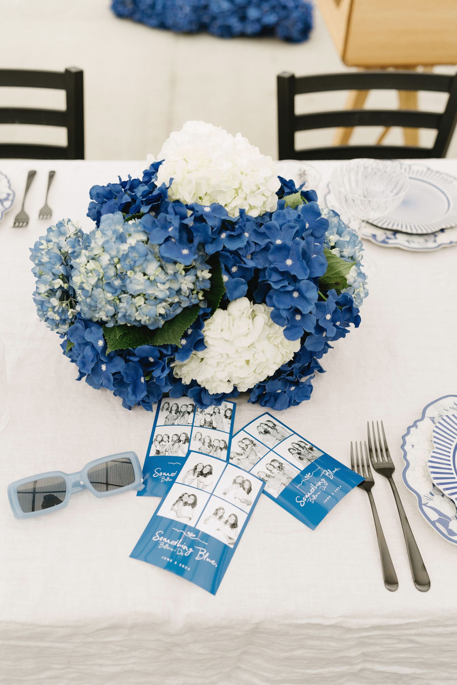 Place settings with blue hydrangea centerpieces and custom photo cards on a white tablecloth.