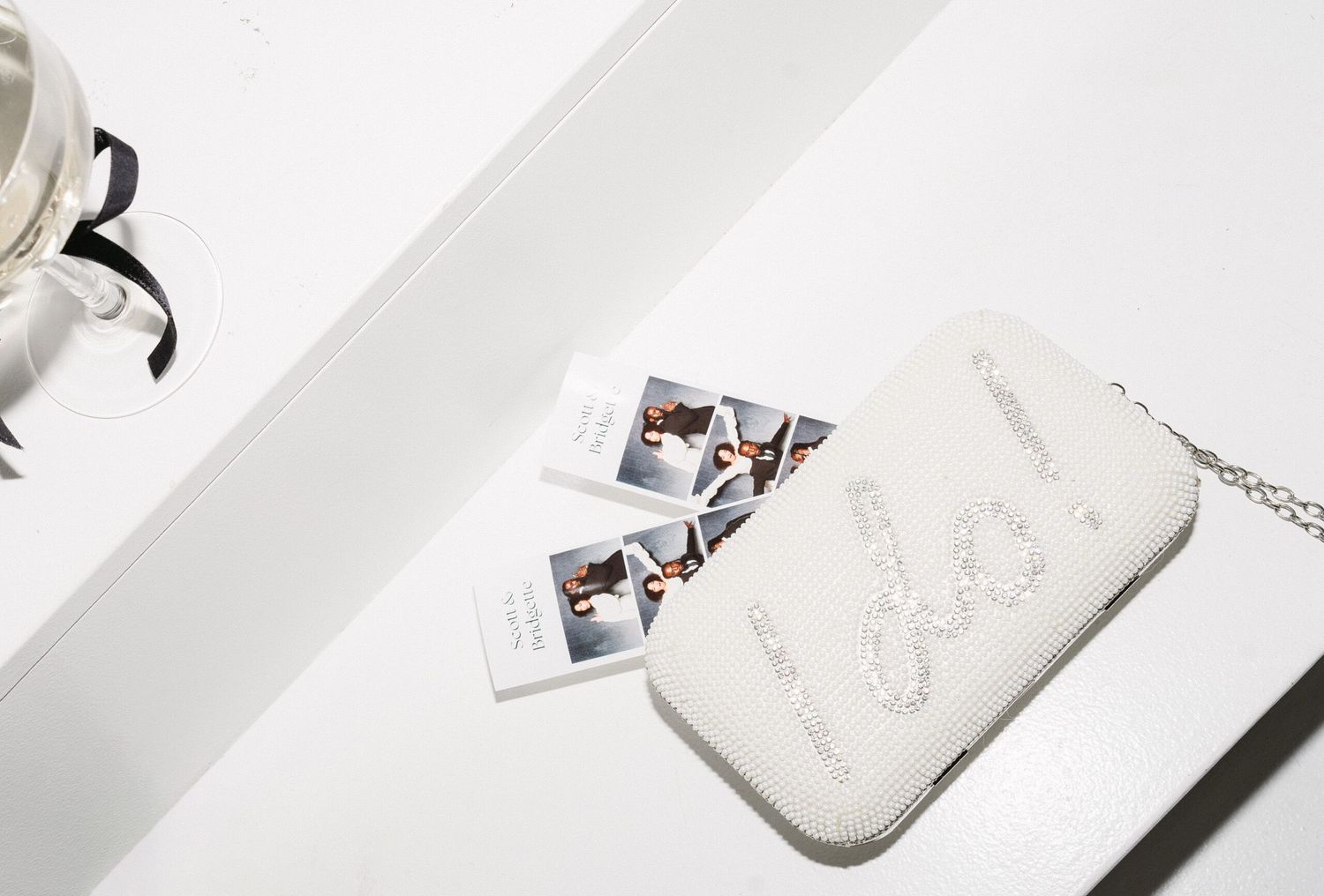 White sparkly clutch bag with photo strips and chain detail on minimalist background.