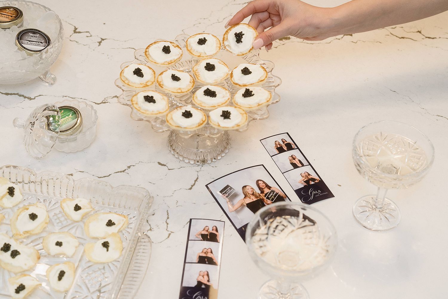 Hand placing frosted Halloween eyeball sugar cookies on a white marble counter with champagne glasses and photos nearby.