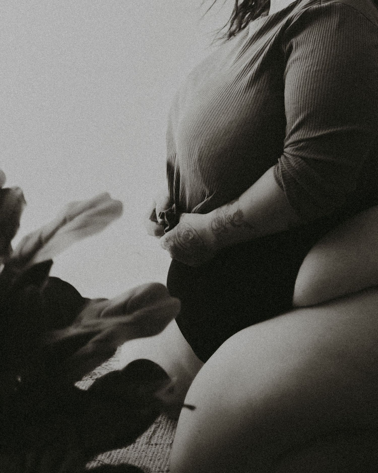 Black and white artistic photo of a person in a ribbed sweater sitting on a soft surface in moody lighting.