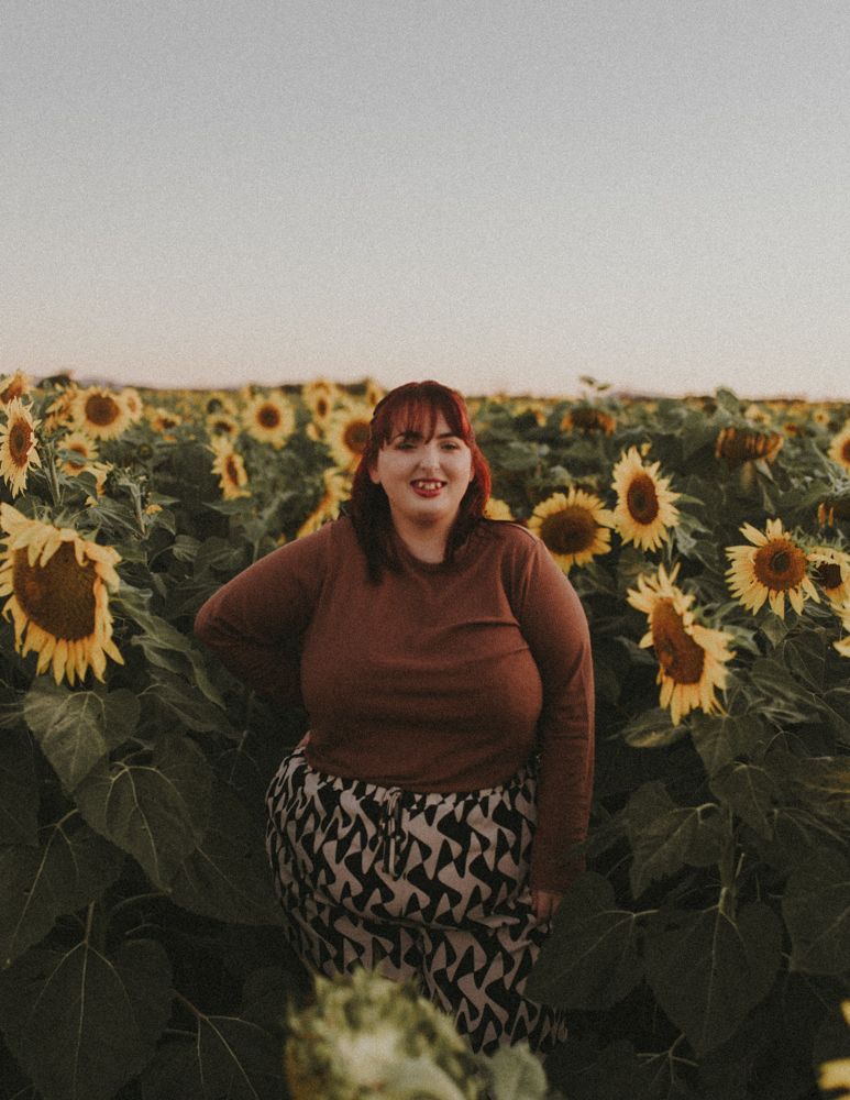 Person in casual attire smiling while standing in a vibrant sunflower field.