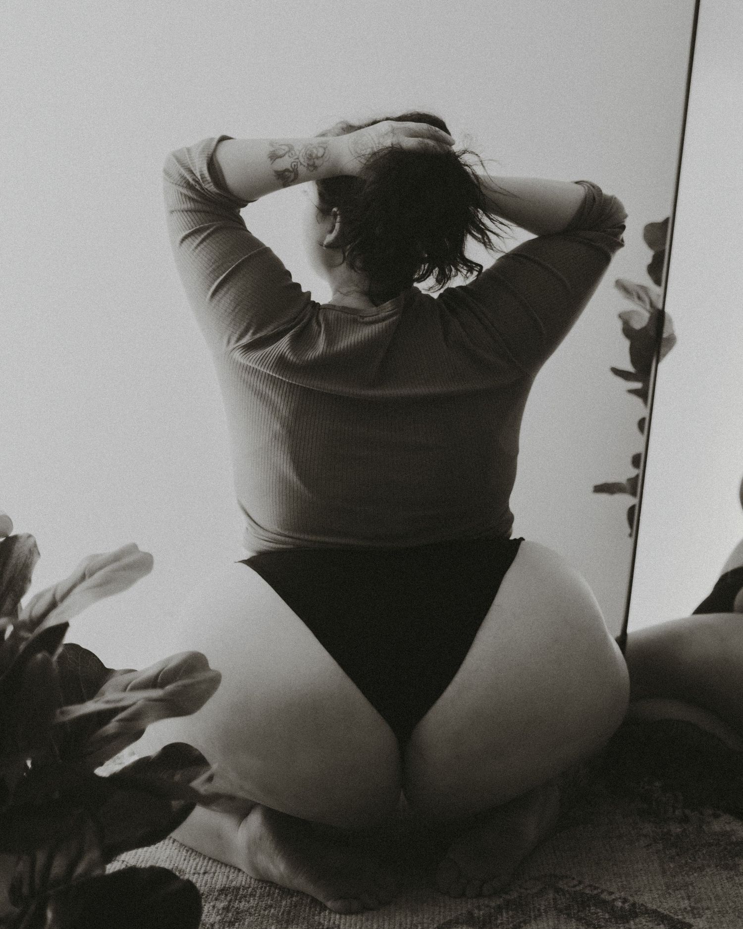 Artistic black and white portrait of a person in a bodysuit sitting with their back facing the camera.