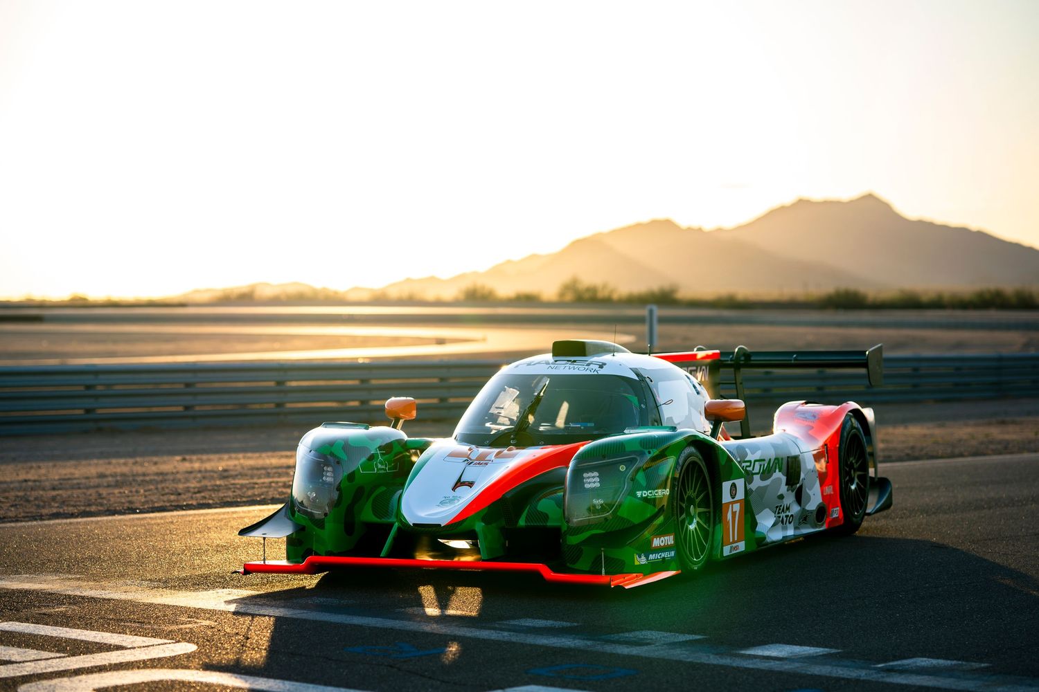 Racing cars positioned on track during golden hour with mountain silhouettes in background.