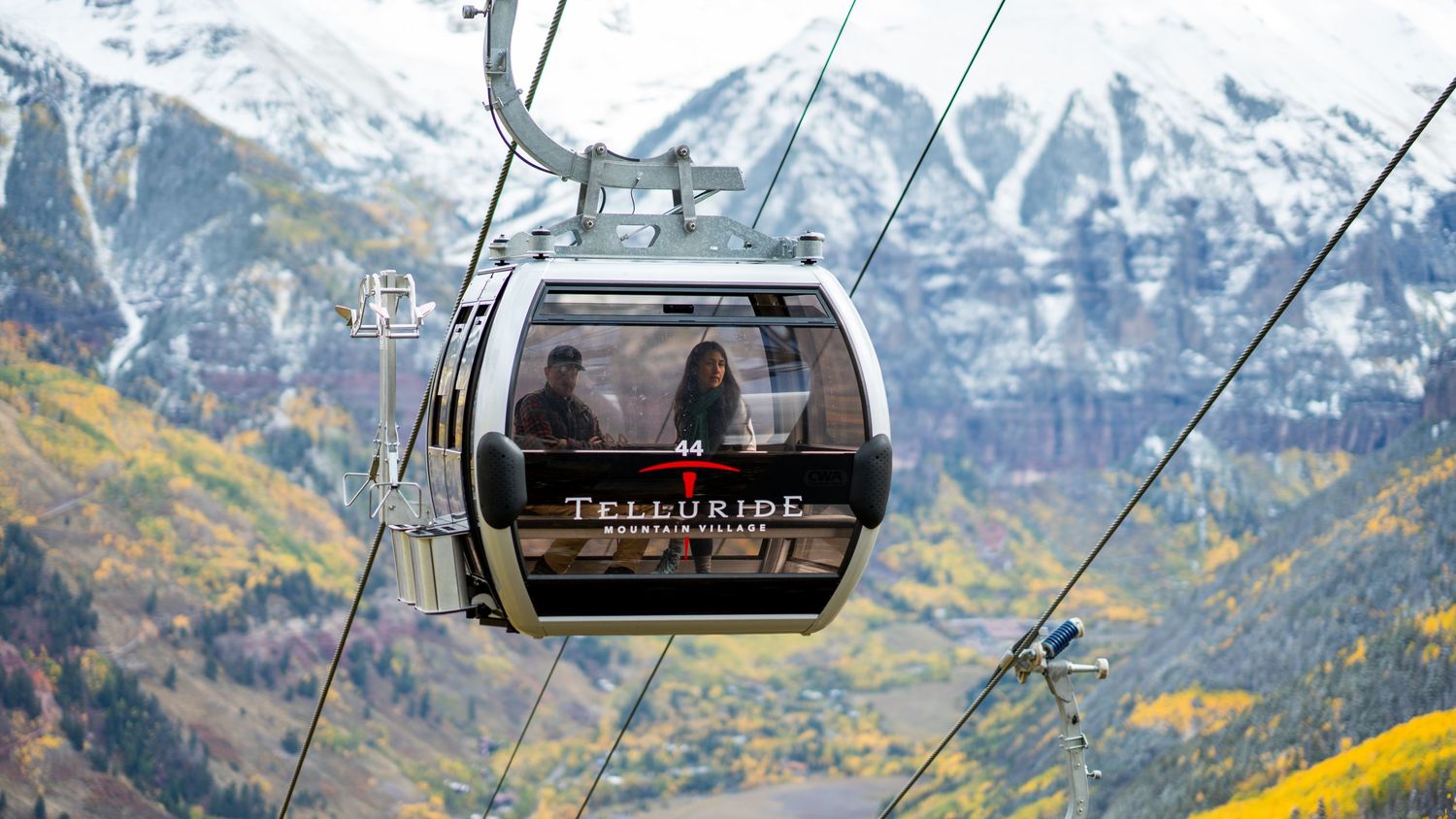 Telluride gondola cabin suspended over mountain valley with snow-capped peaks and autumn colors.