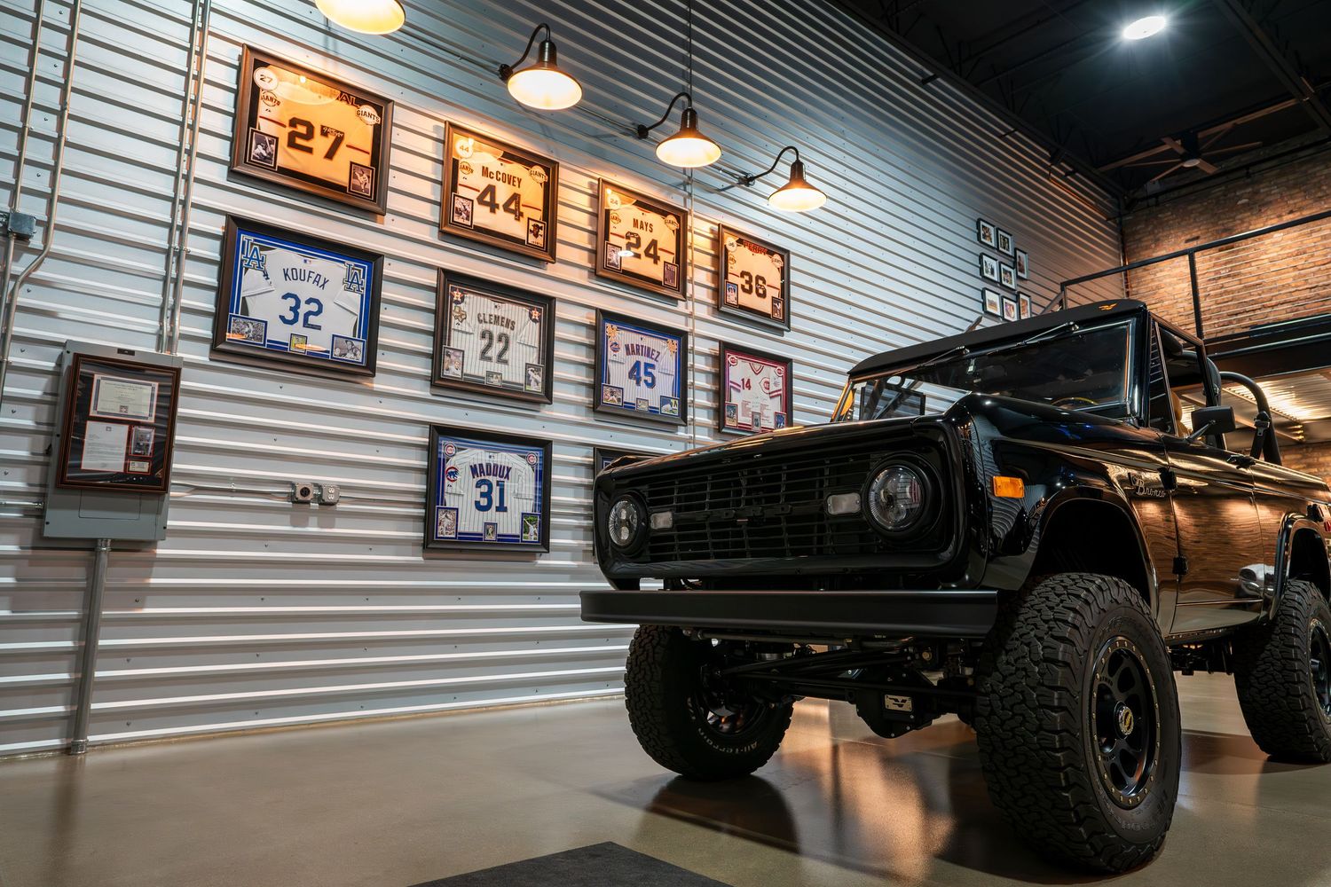 Custom garage showroom featuring a lifted black Bronco and automotive artwork on display wall.