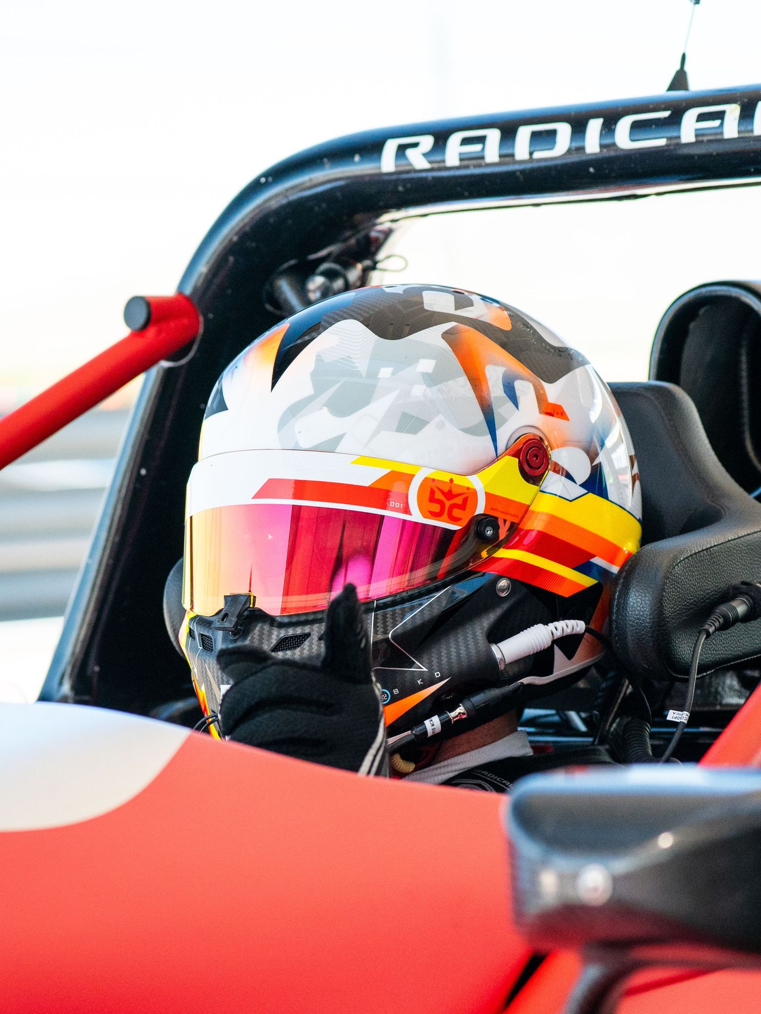 Racing helmet inside Radical sports car cockpit with red and white color scheme.