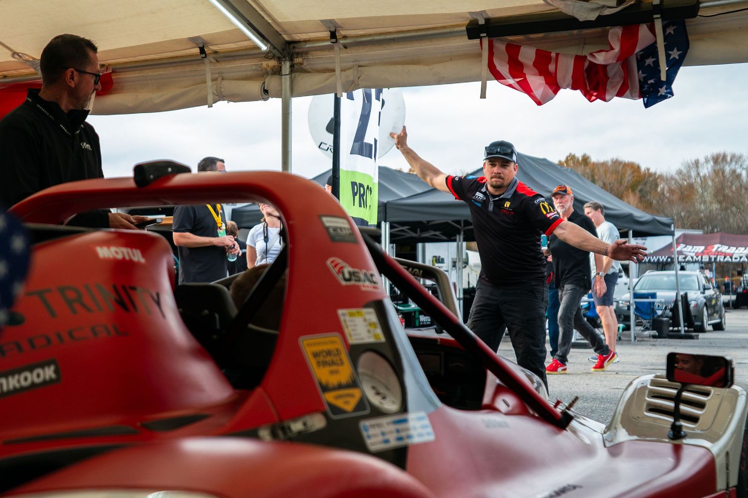 Racing team mechanics performing maintenance checks in an outdoor pit area.
