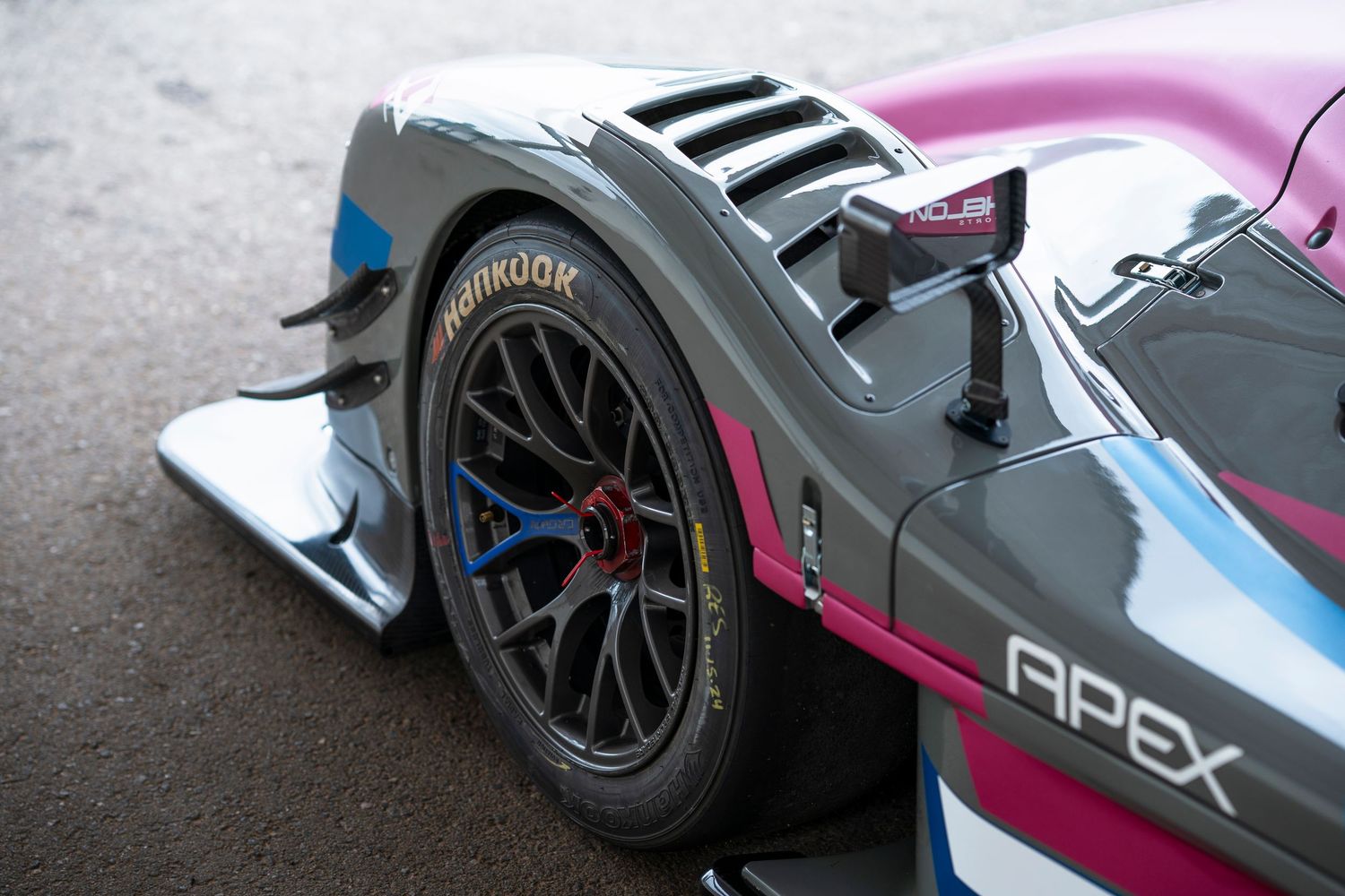 Close-up view of a racing car's wheel and suspension system with pink and blue livery details.