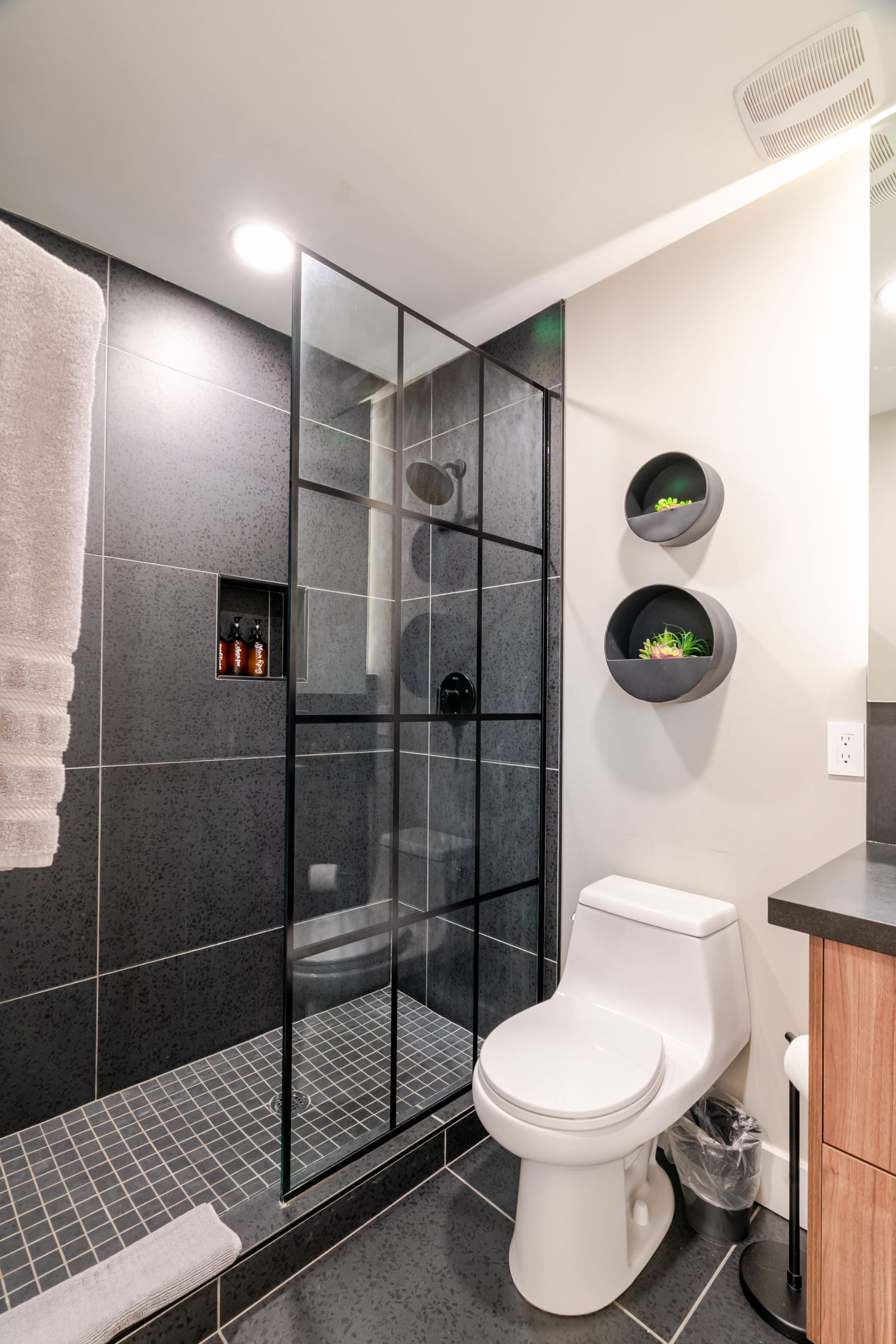 Modern bathroom featuring dark grey tile, glass shower enclosure, and circular wall shelves.