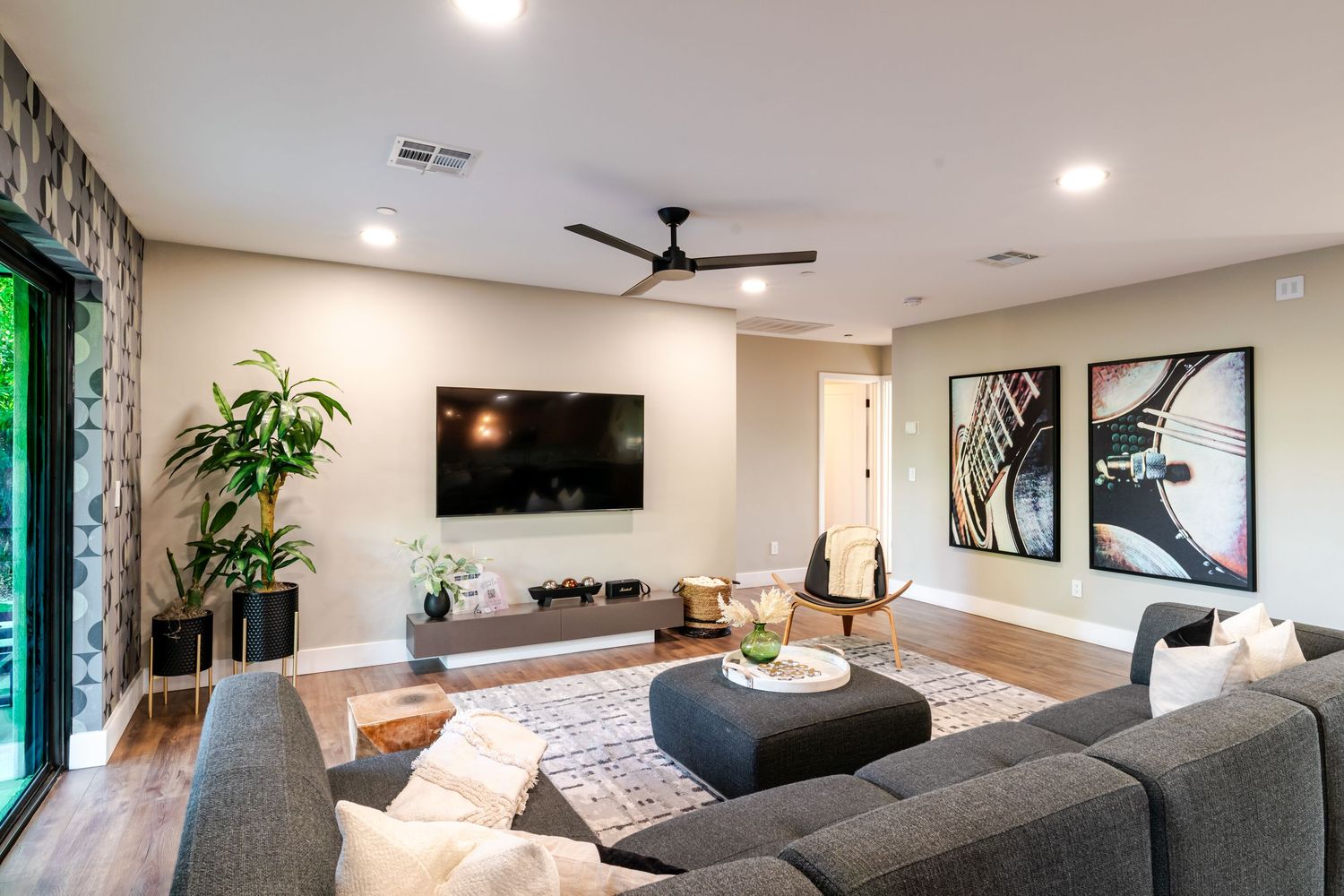 Open concept living area with grey sectional sofa, modern ceiling fan, and large windows overlooking the yard.