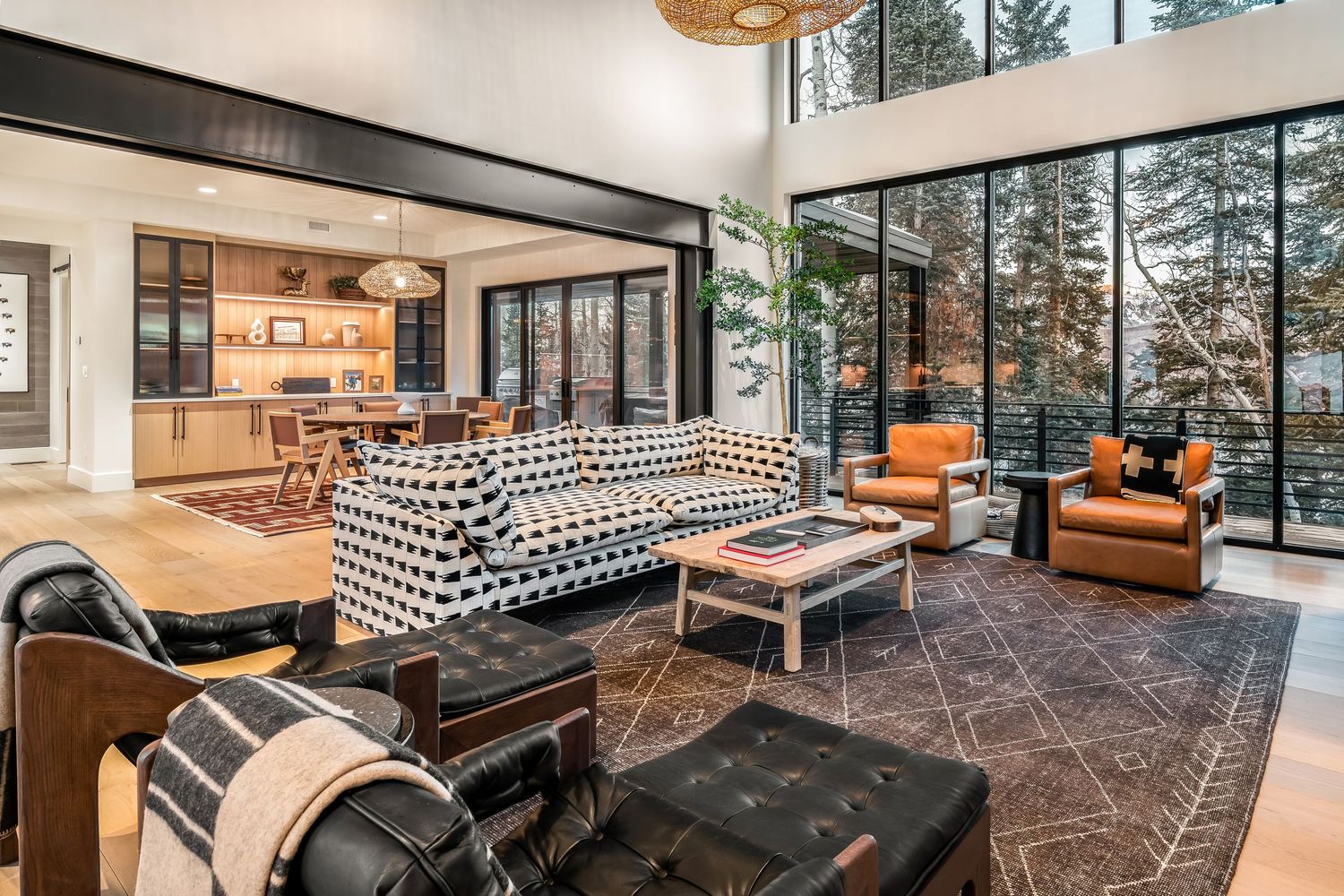 Modern mountain home interior features floor-to-ceiling windows, geometric rugs, and contemporary furnishings in an open layout.