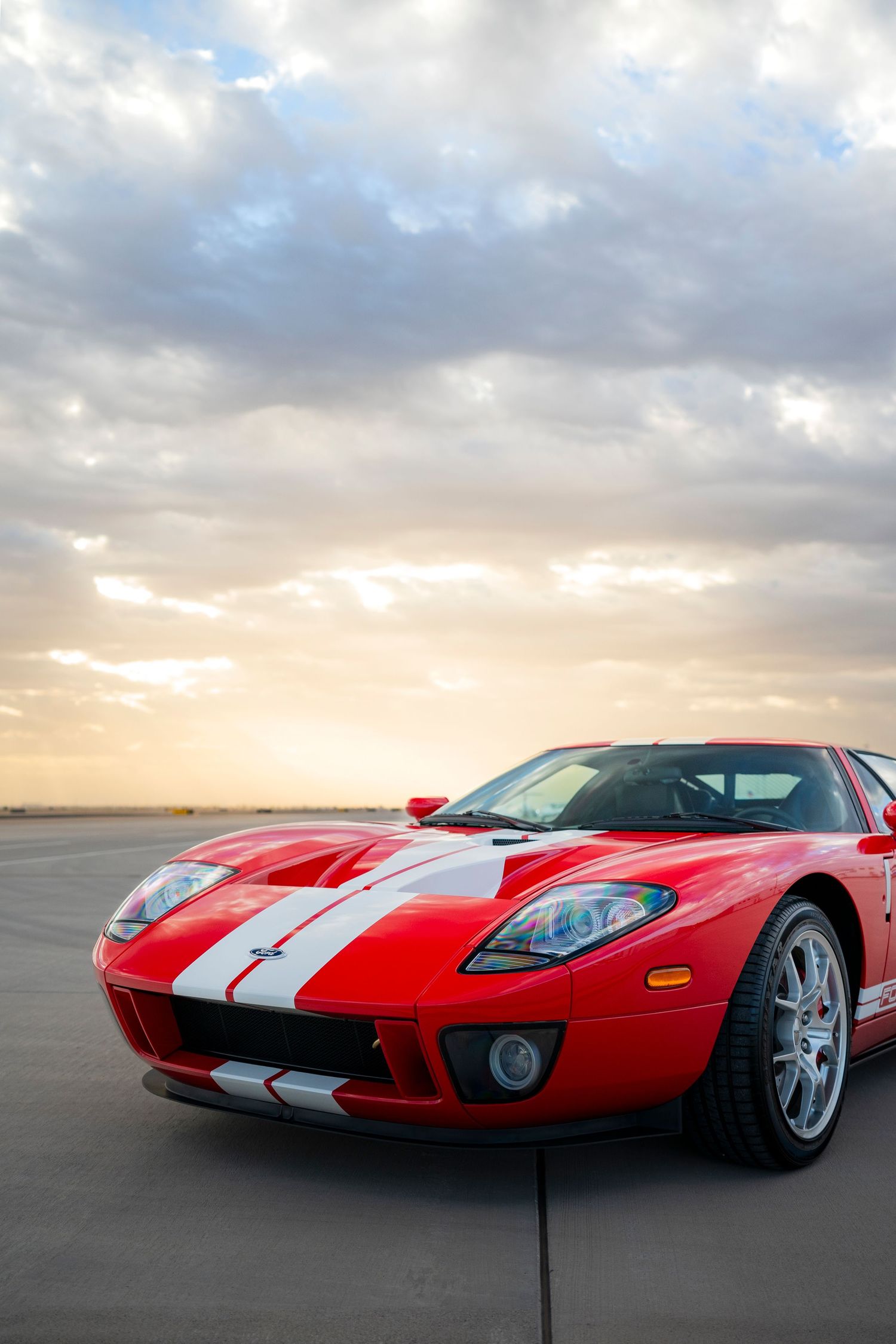 Ford GT supercar in classic red and white livery against sunset sky.