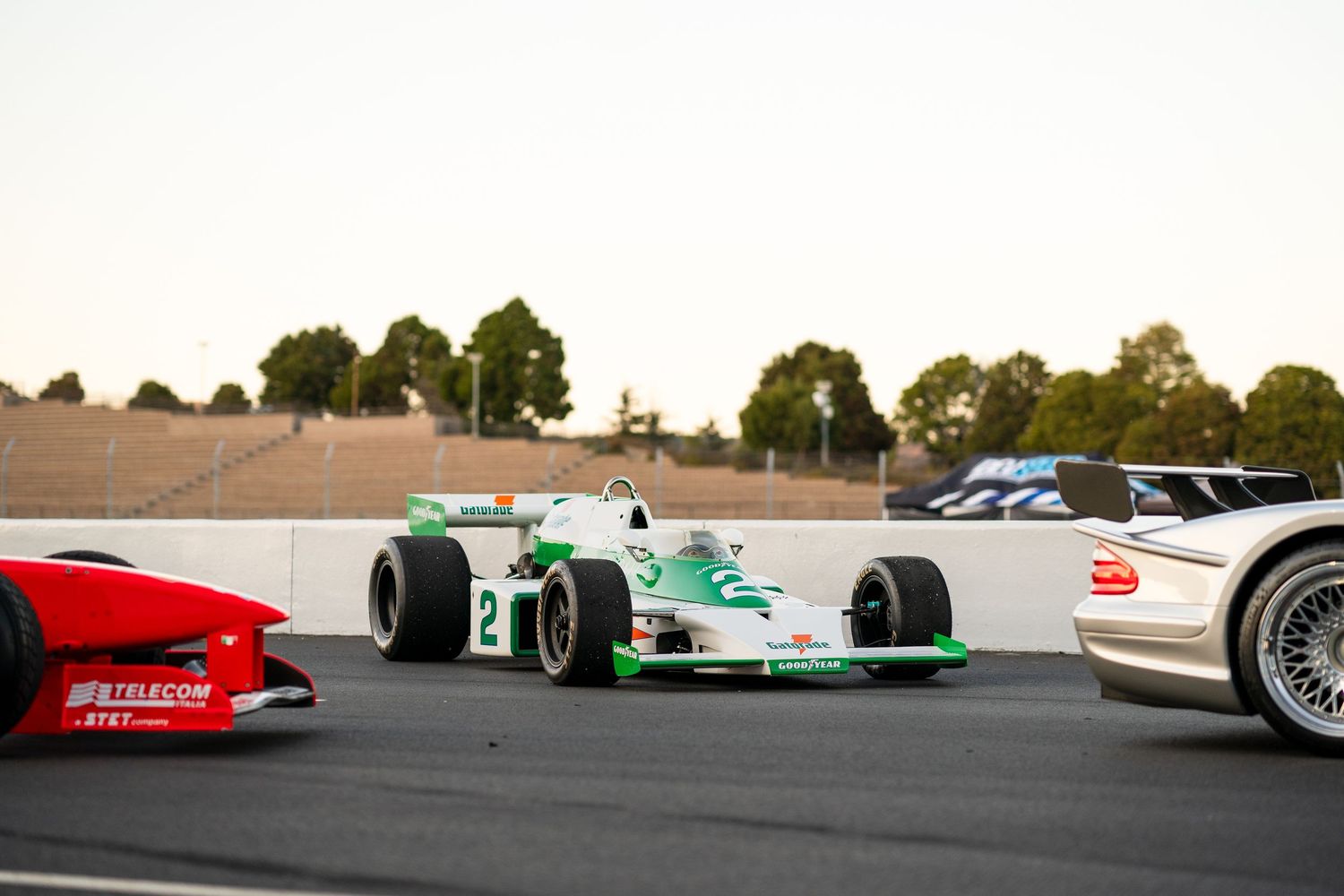 A series of racing cars lined up on a track with trees visible in the background.