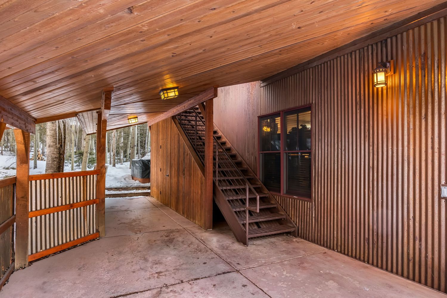 Covered walkway with wooden ceiling and metal railings leading to interior staircase in mountain home.