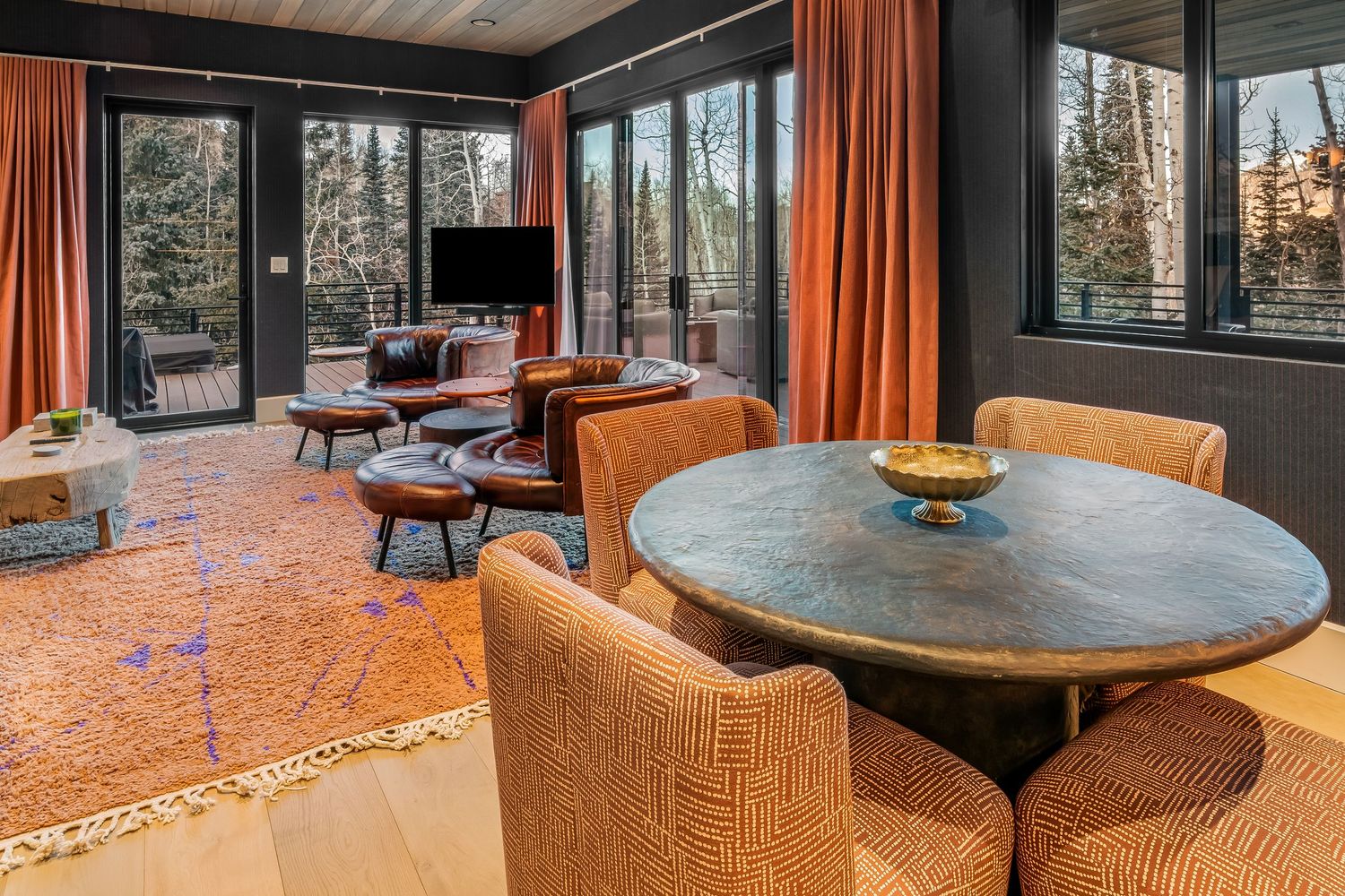 Open concept living space with orange accents and floor-to-ceiling windows offering forest views.