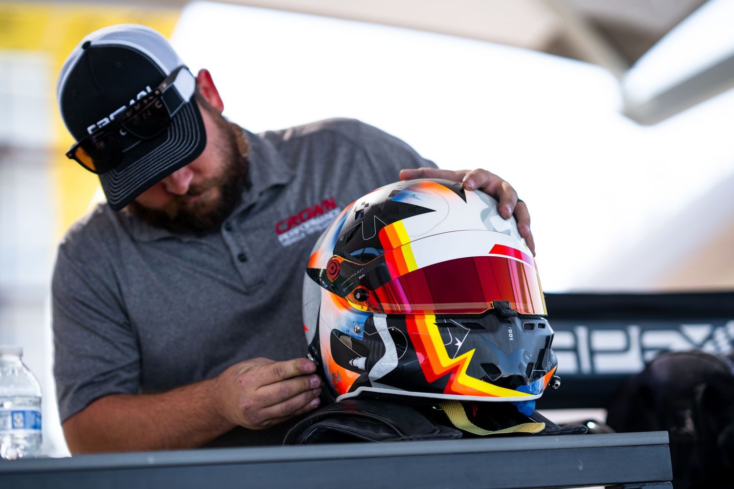 Mechanic inspects and adjusts racing helmet with vibrant orange and red design.