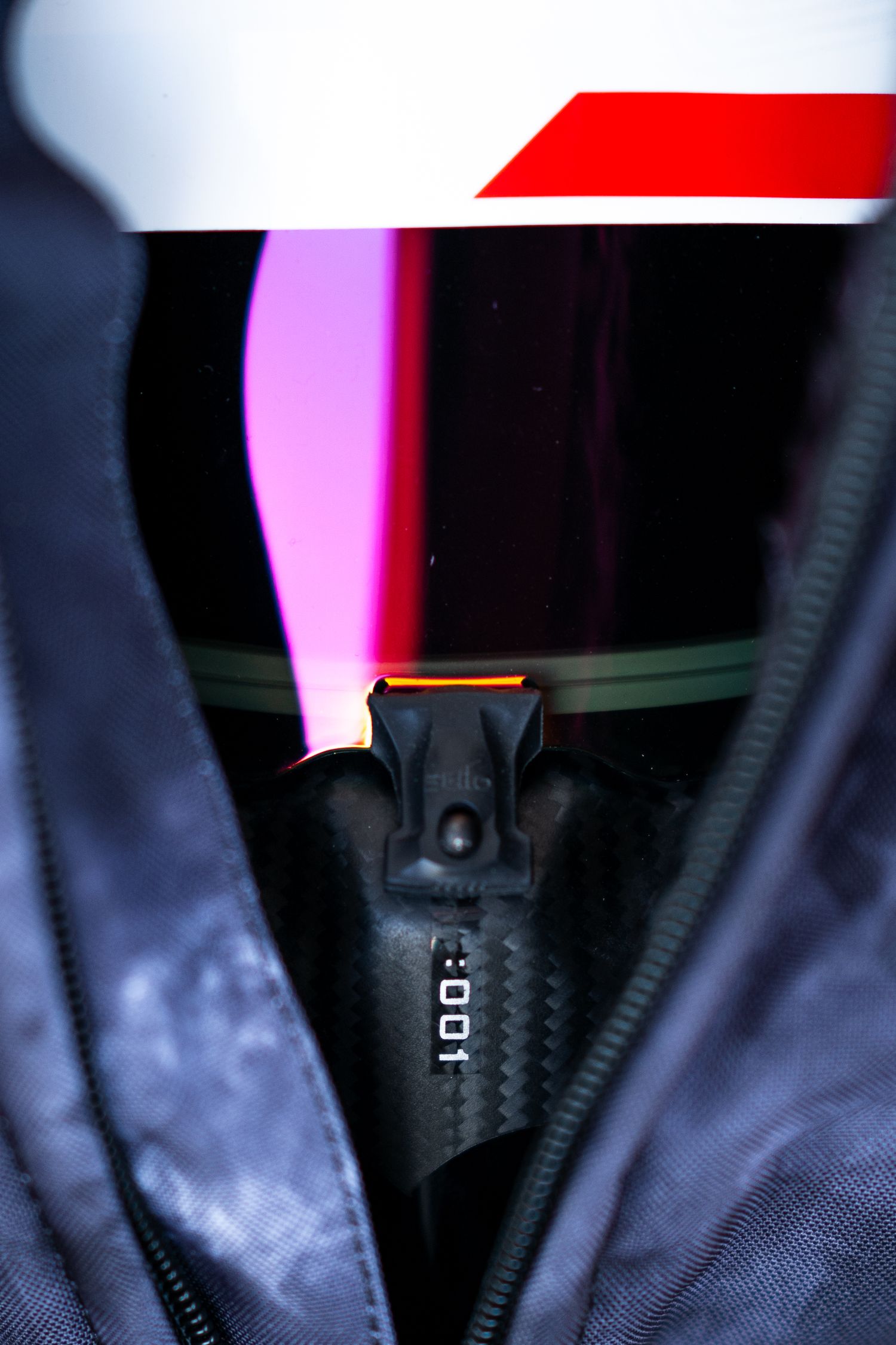 Close-up of racing helmet visor showing pink reflection and zipper detail.