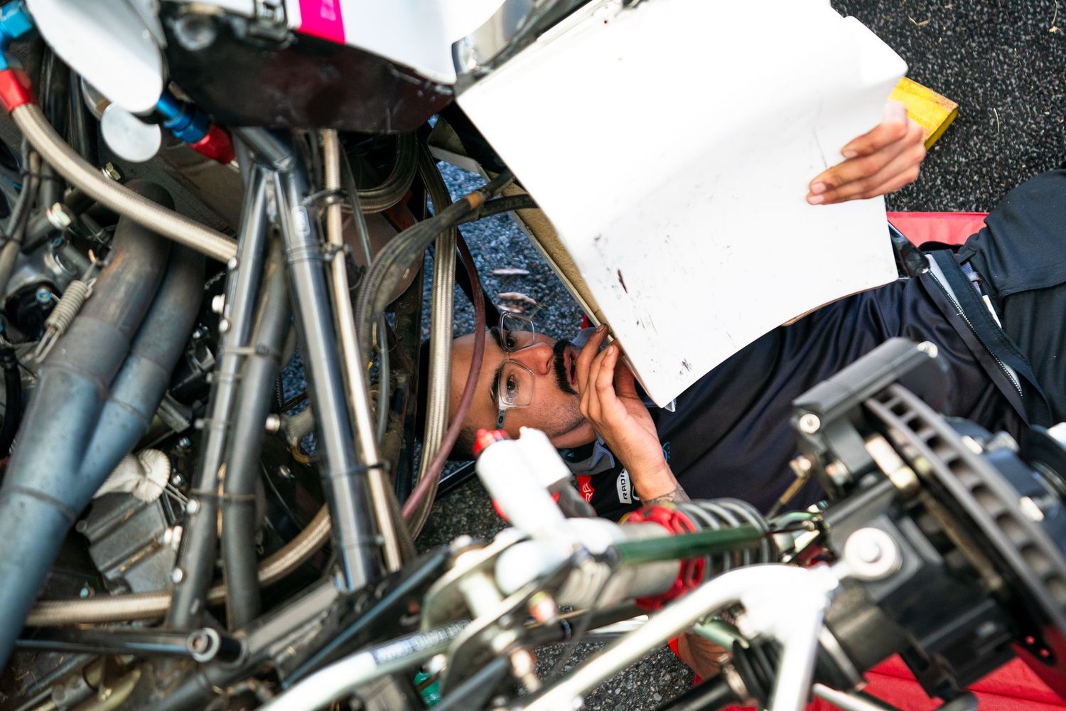 Close-up view of race car mechanics working under the hood during maintenance.